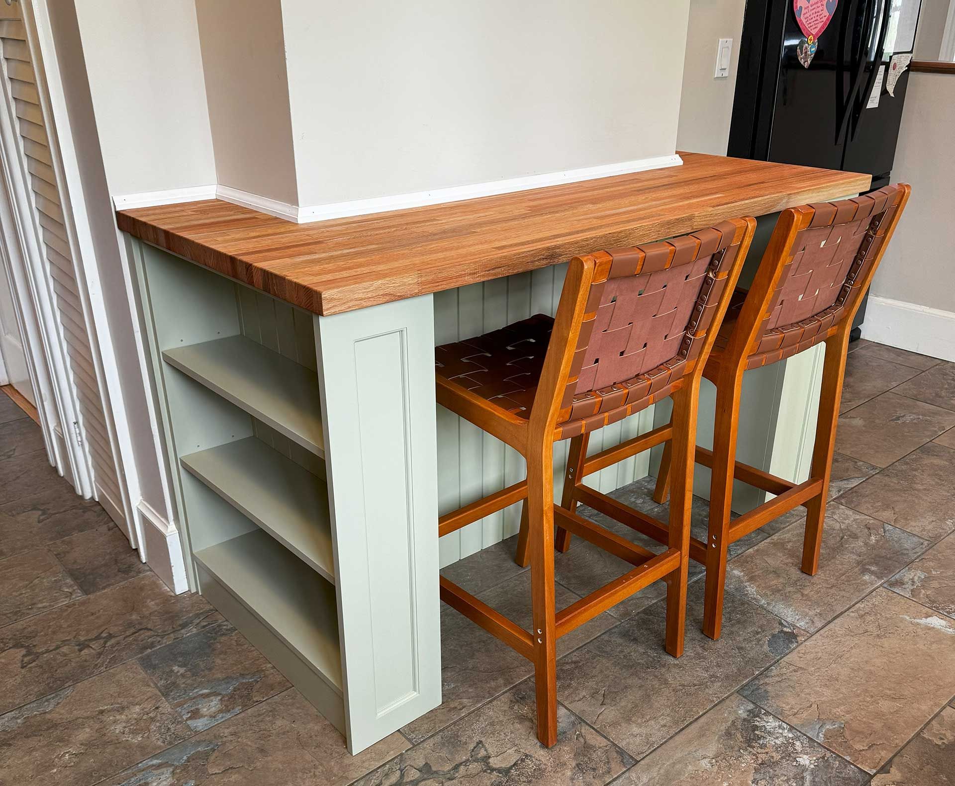 Countertop with two bar stools. Built-in shelves on one side, light wood top, seats with studded backs.