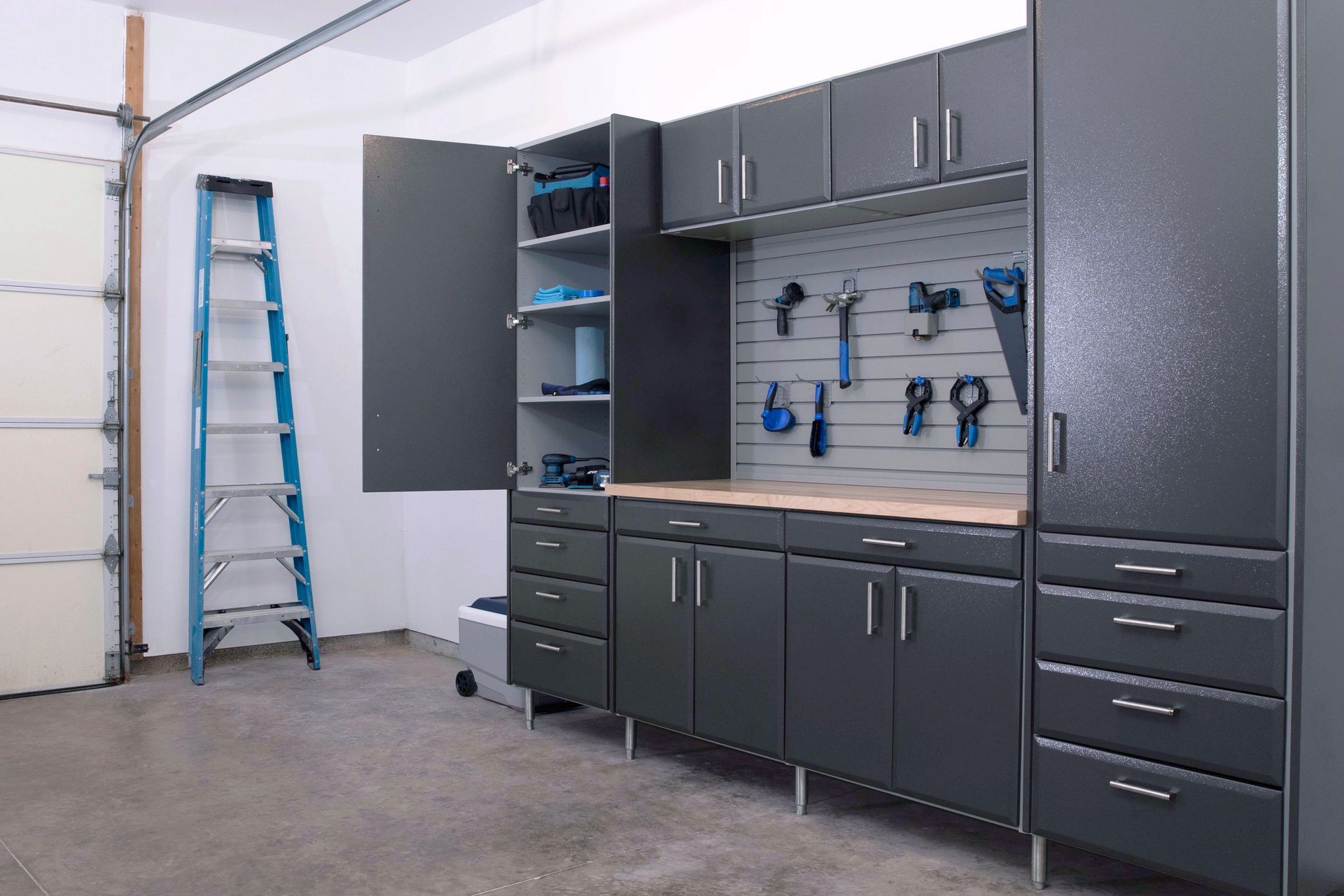 Garage with dark gray cabinets, pegboard, workbench, tools, and a ladder.
