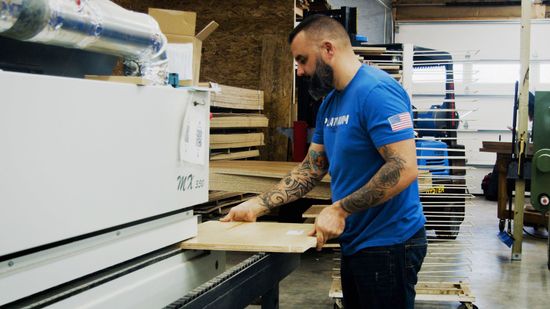 Man working with a machine in a workshop, placing a wooden board.