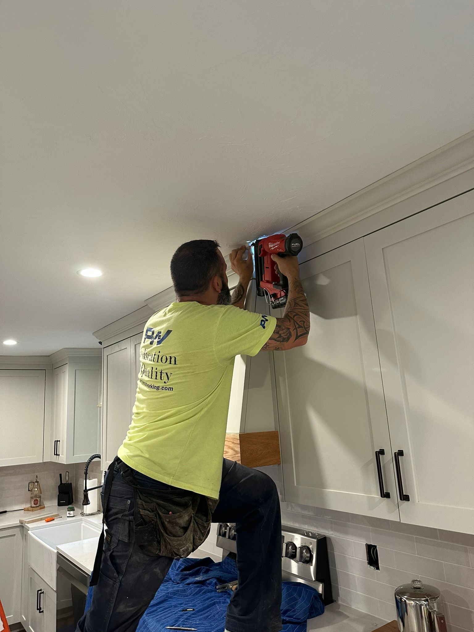 Man on a step stool using a nail gun to install trim on kitchen cabinets.