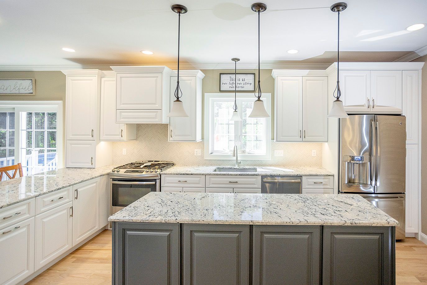 Kitchen with white cabinets, gray island, granite countertops, stainless steel appliances, and pendant lights.