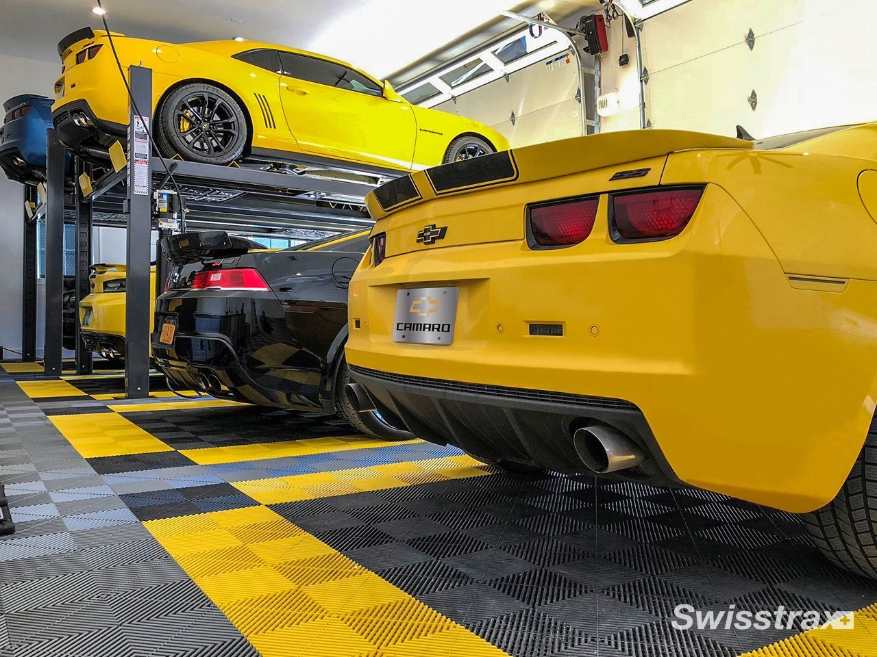 Yellow Camaros and a black car parked in a garage with black and yellow flooring.