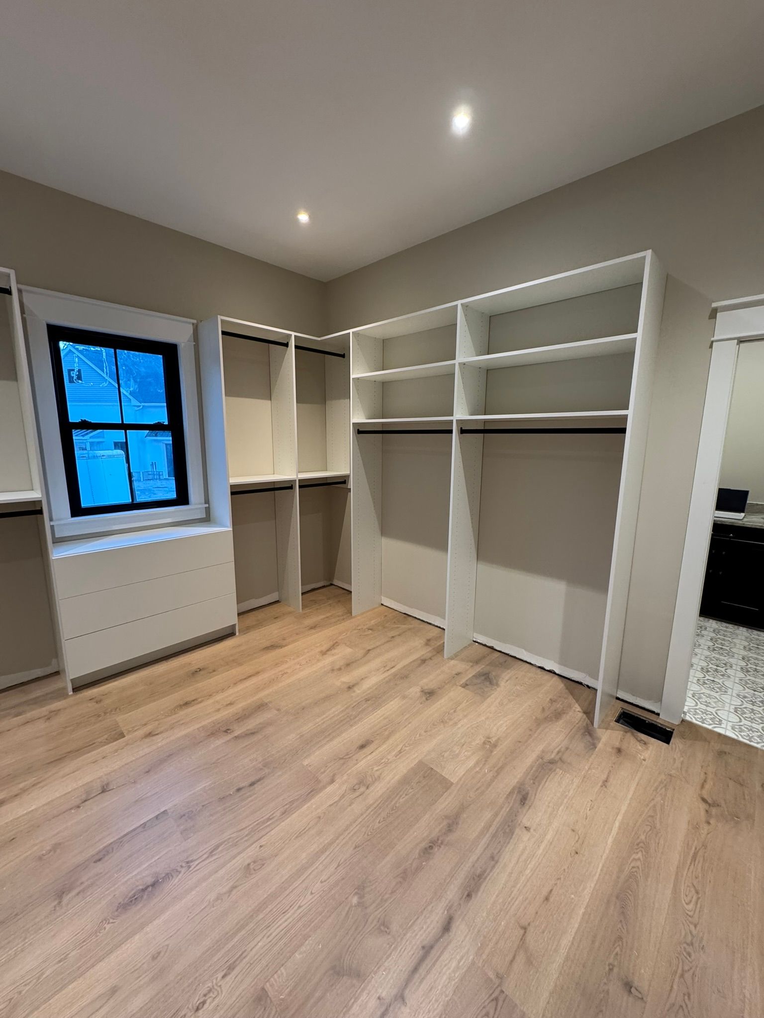 Empty walk-in closet with white shelving, a window, and wooden flooring.