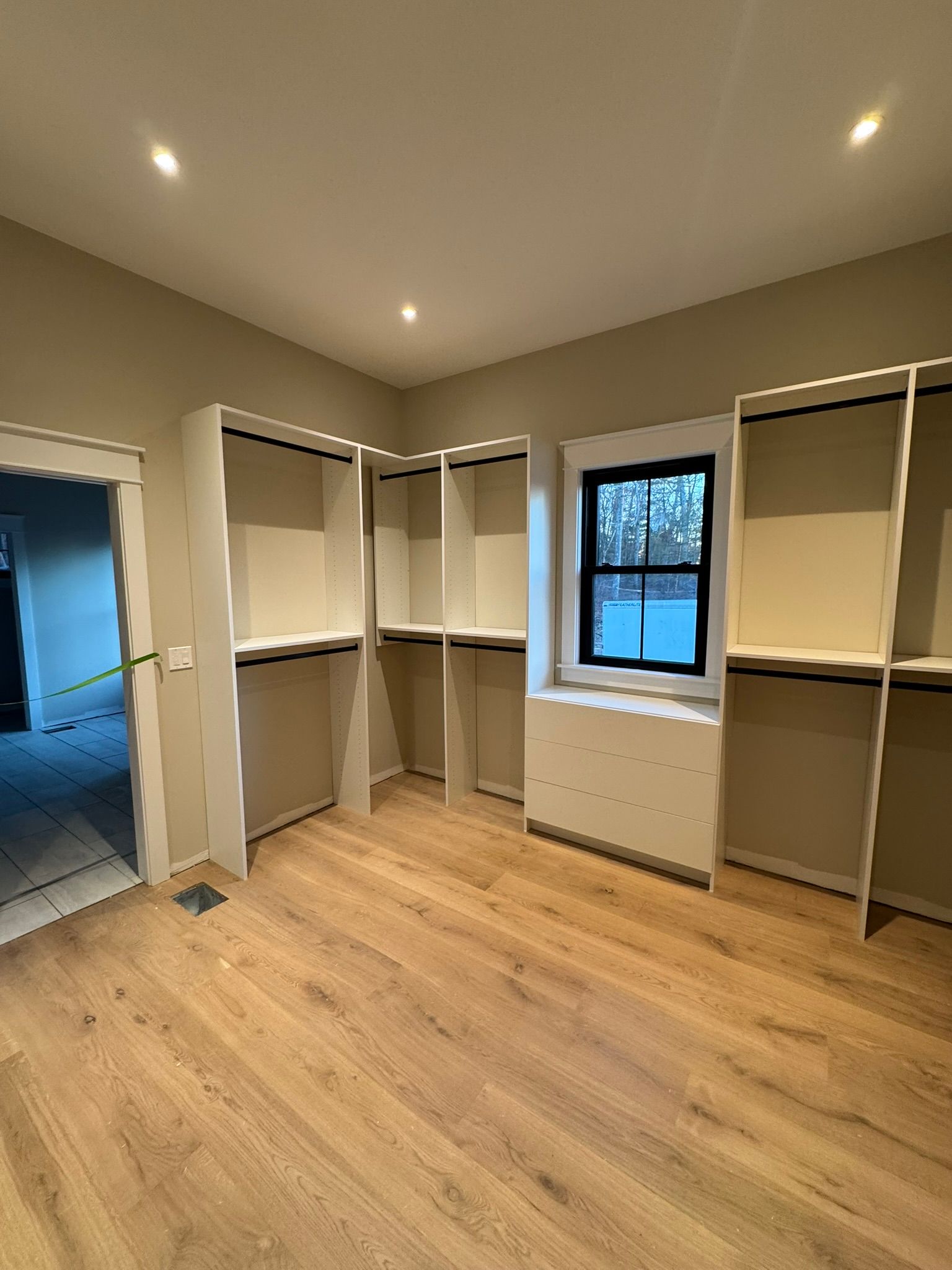 Empty walk-in closet with built-in shelving and a window. Light wood flooring and neutral walls.