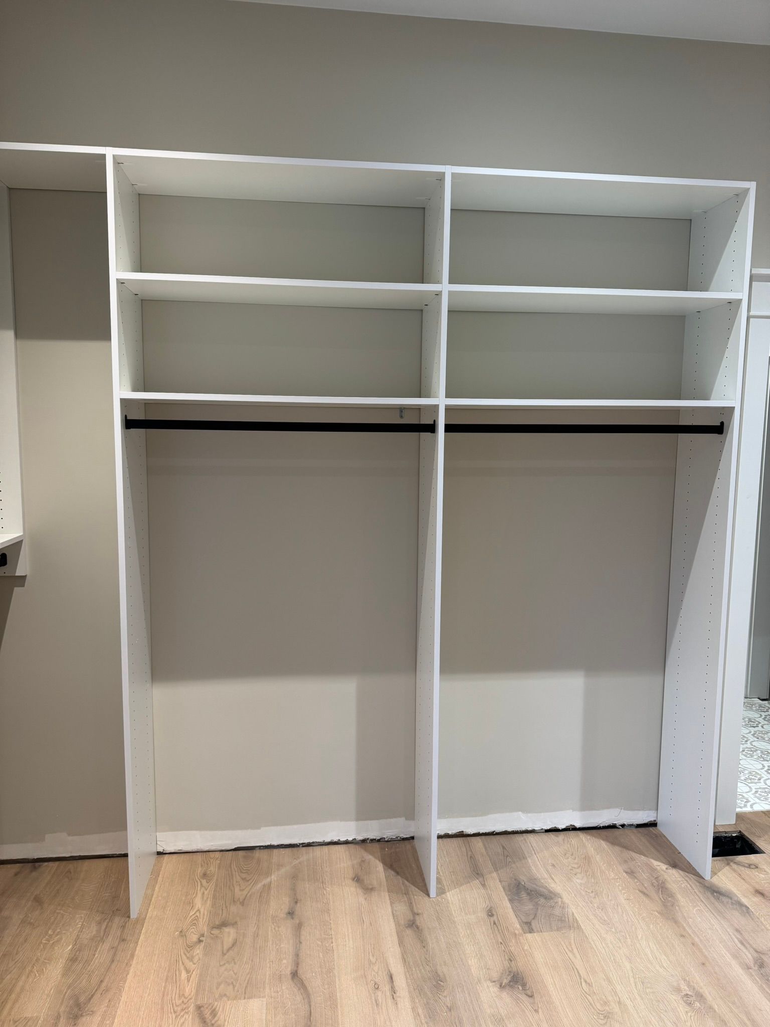 White closet organizer with shelves and a hanging rod, set against a light gray wall.