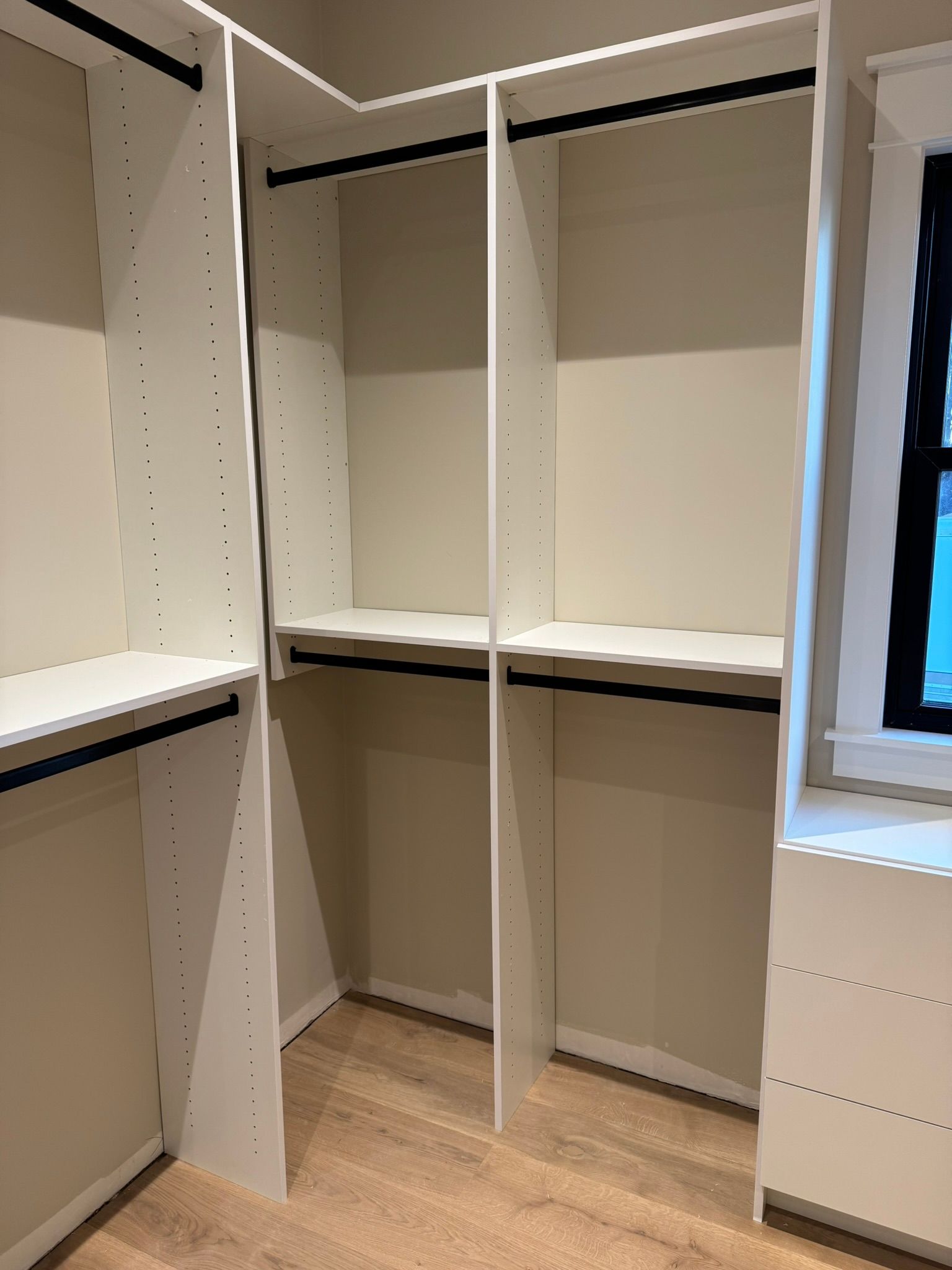 White closet shelving with black rods, in a neutral-toned room.