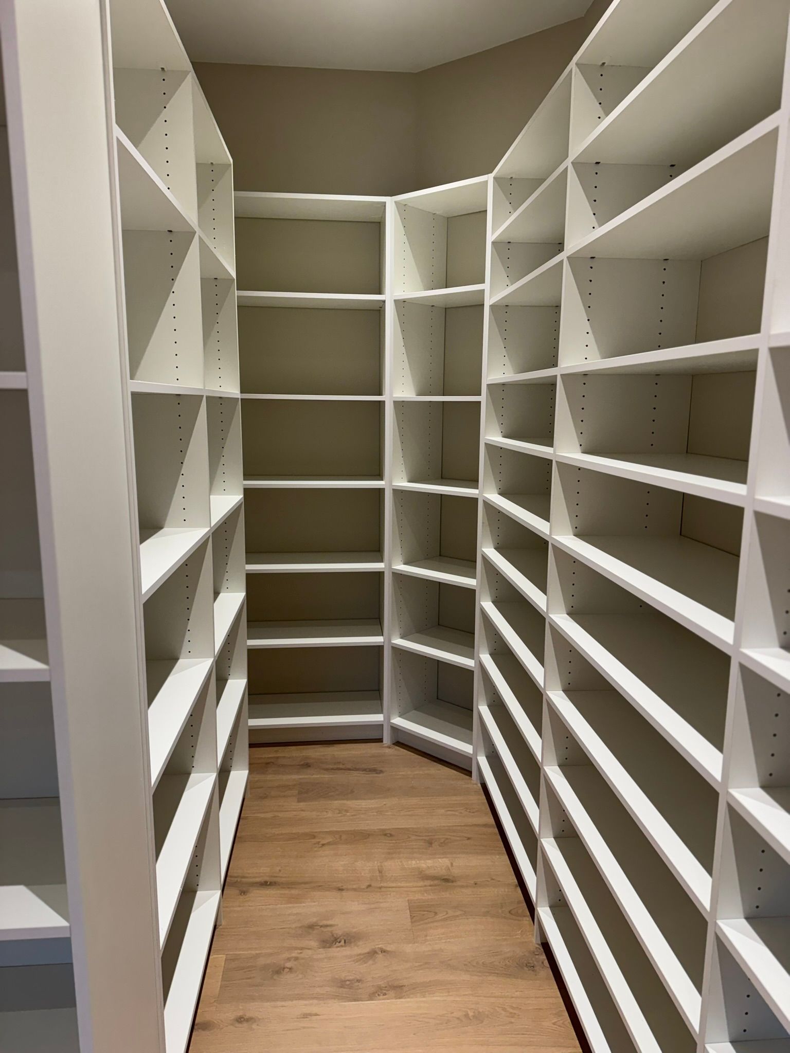 Empty white built-in shelves in a closet with light wood flooring.