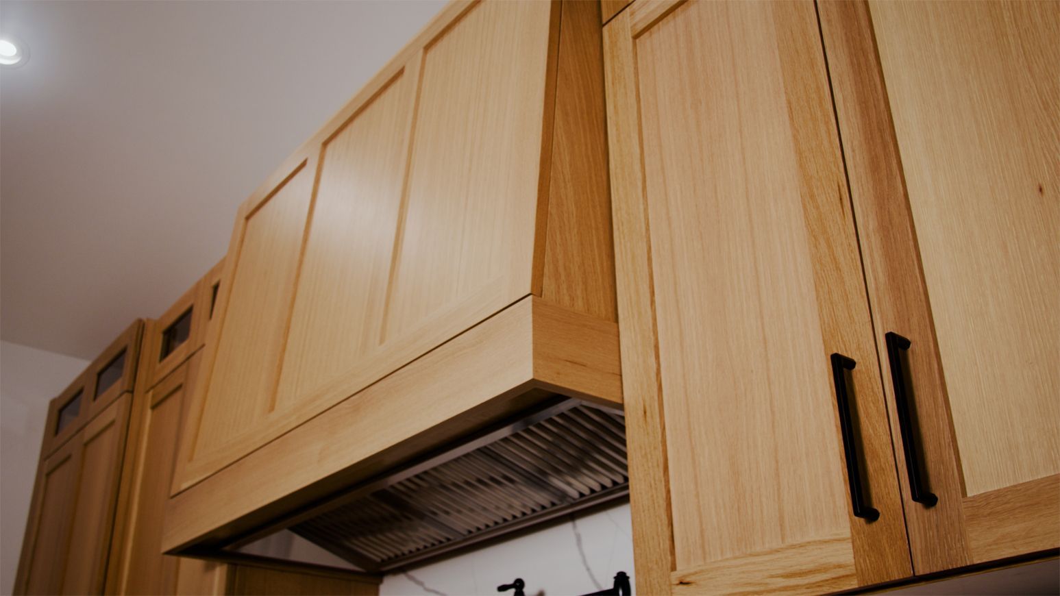 Light wood kitchen cabinets and a matching range hood over a stainless steel range.