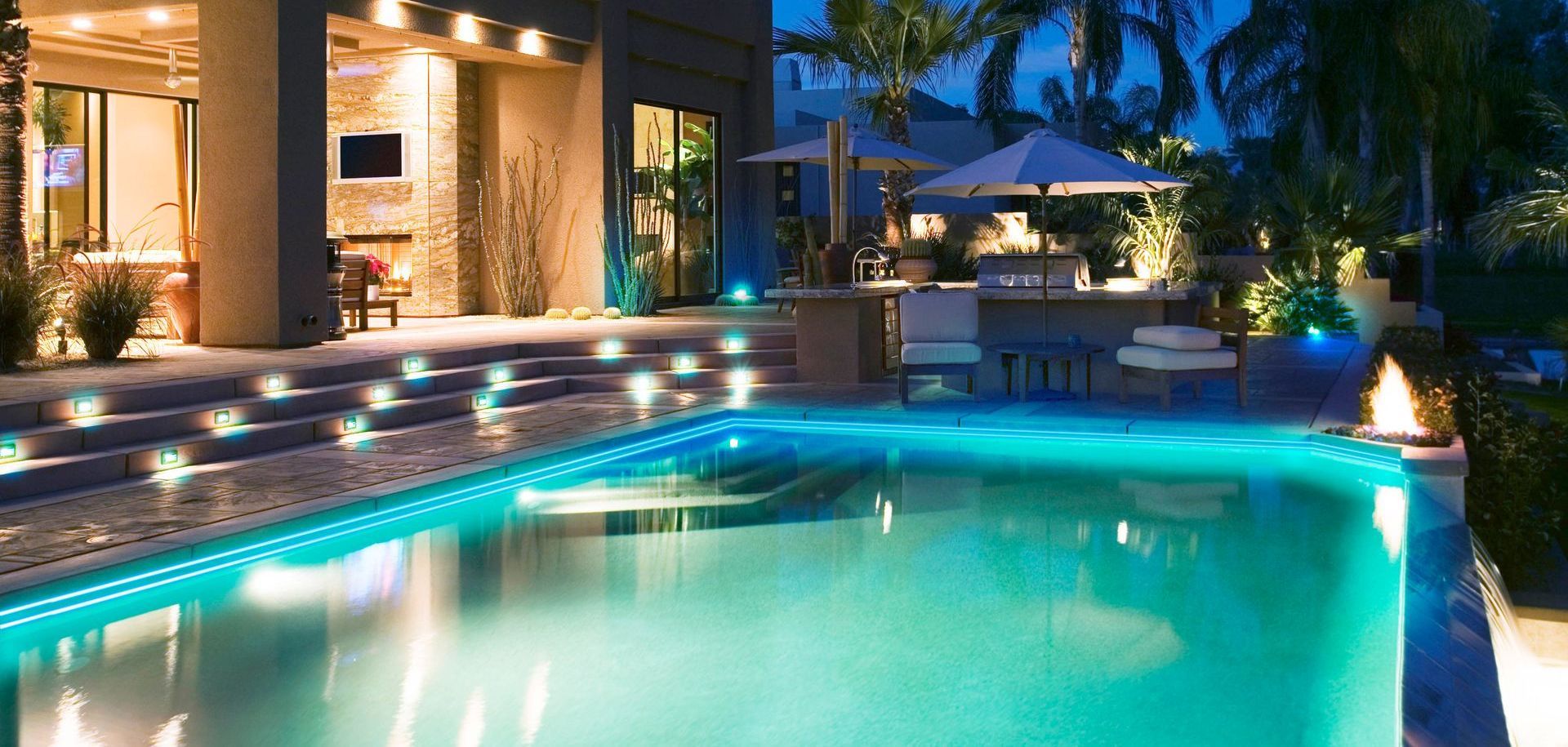 Luxury home exterior at night with illuminated pool and outdoor bar.