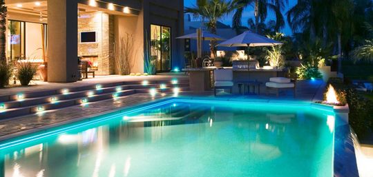 Luxury home exterior at night with illuminated pool and outdoor bar.