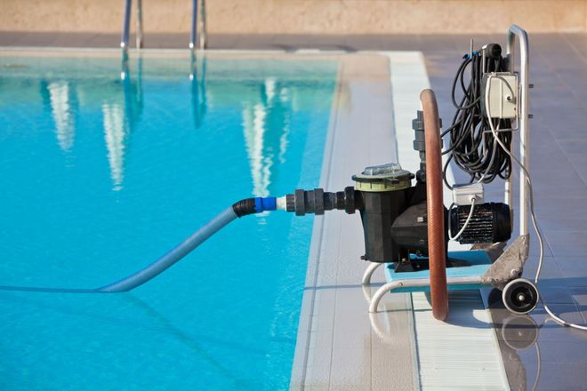 Pool pump system next to a swimming pool with a blue hose in the water.