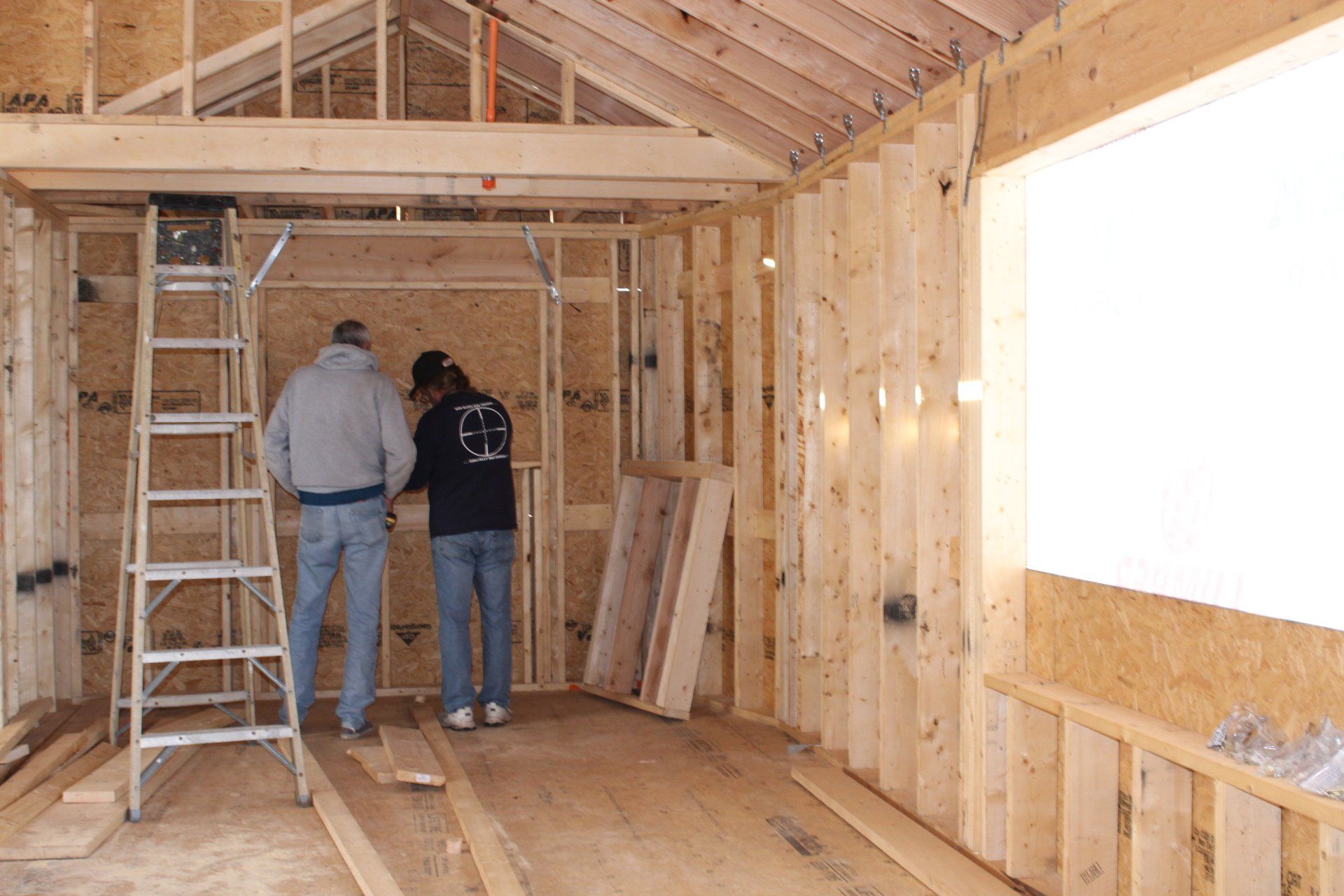 Two men are working on a wooden structure in a room with a ladder