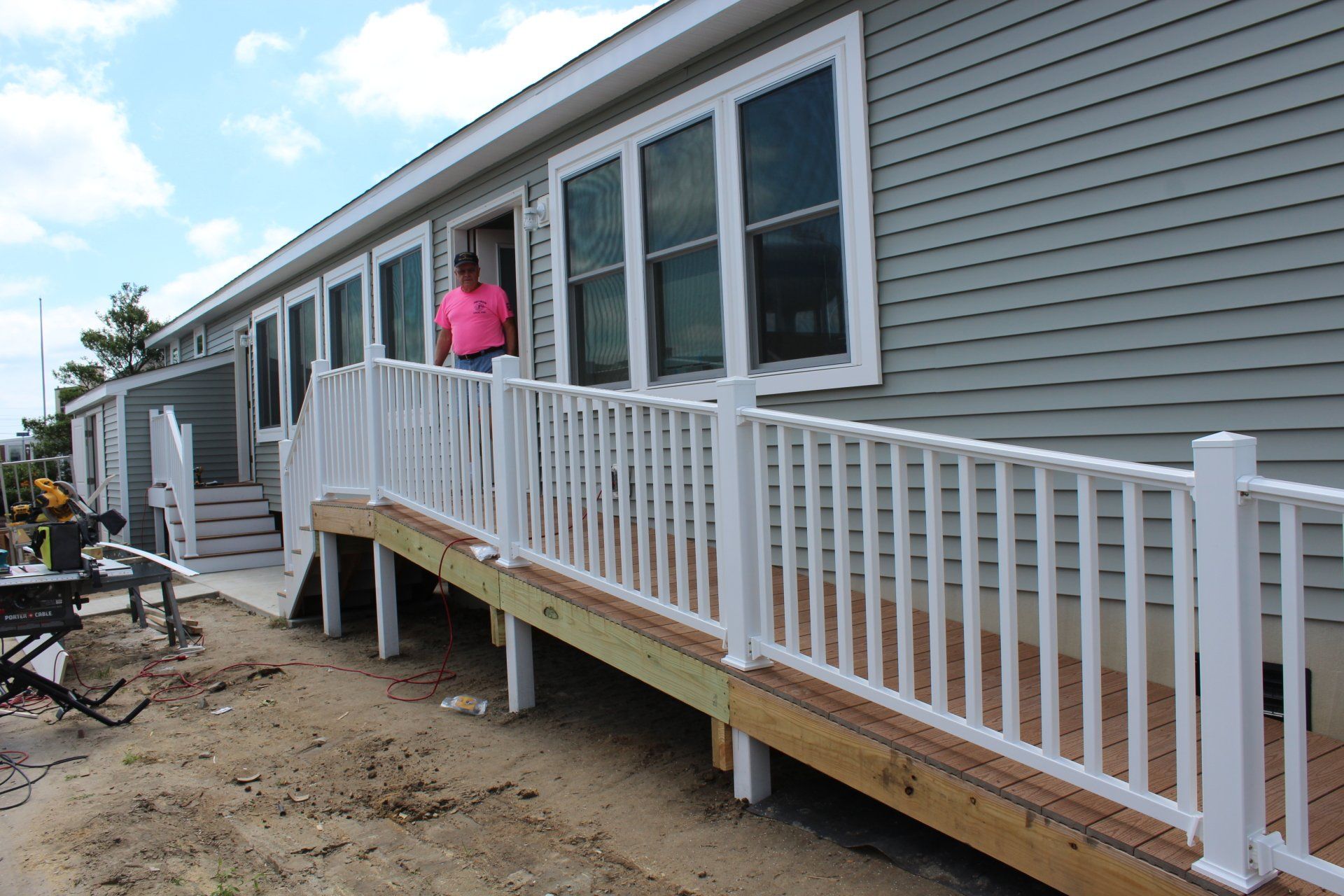 A man in a pink shirt is standing in front of a mobile home with a ramp