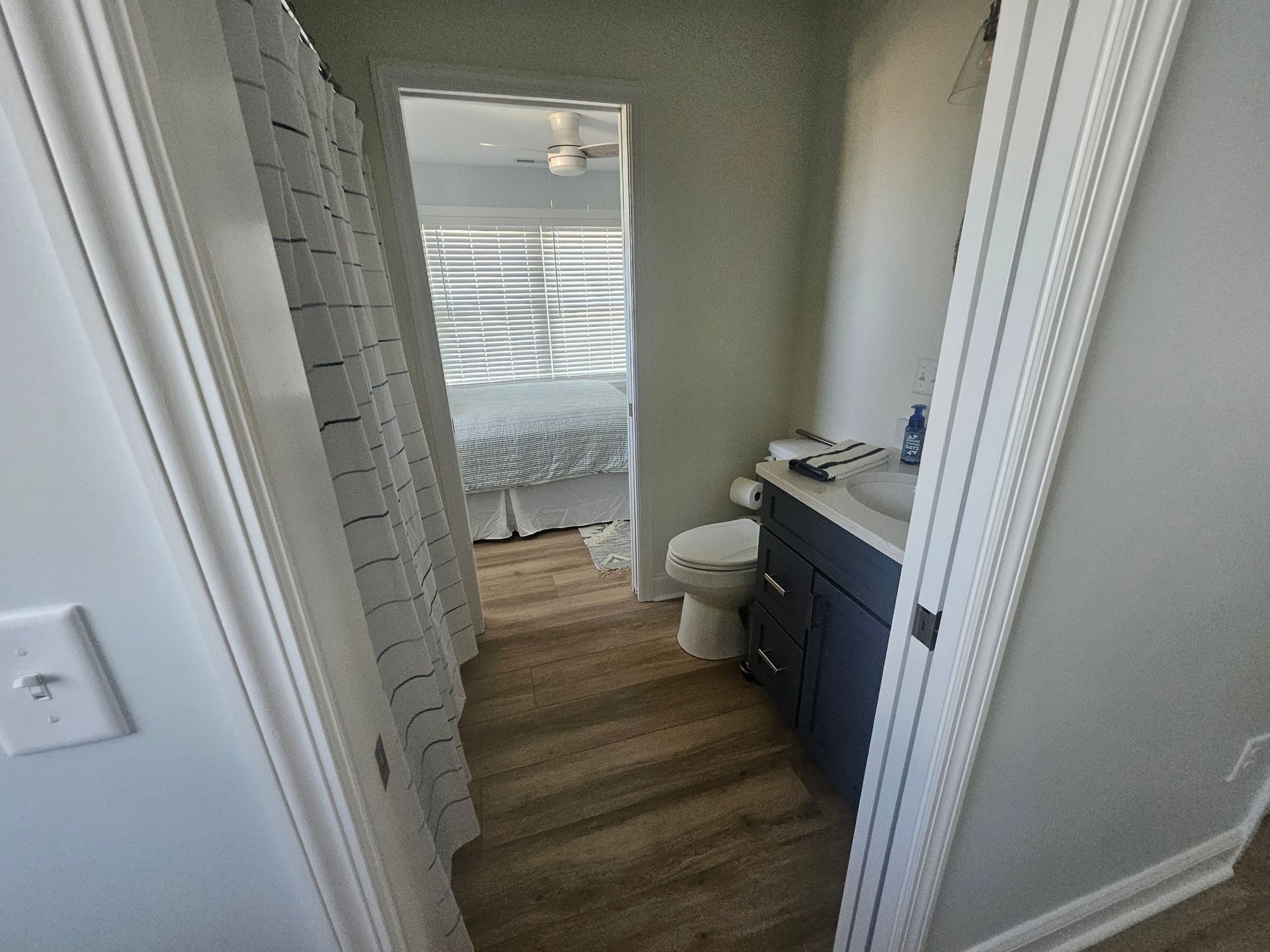 A bathroom with a toilet, sink, and shower curtain leading to a bedroom