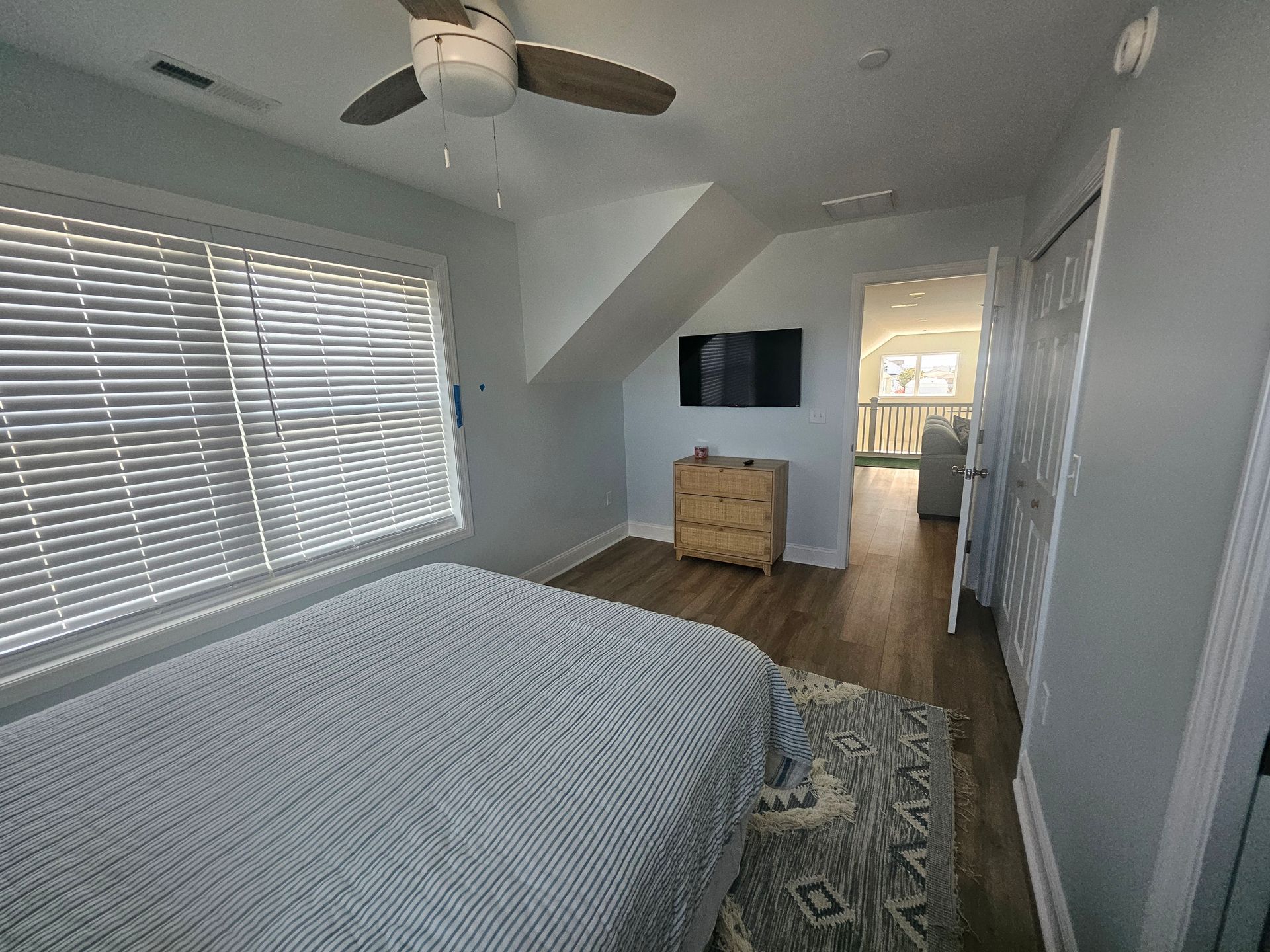 A bedroom with a bed, ceiling fan, television and blinds