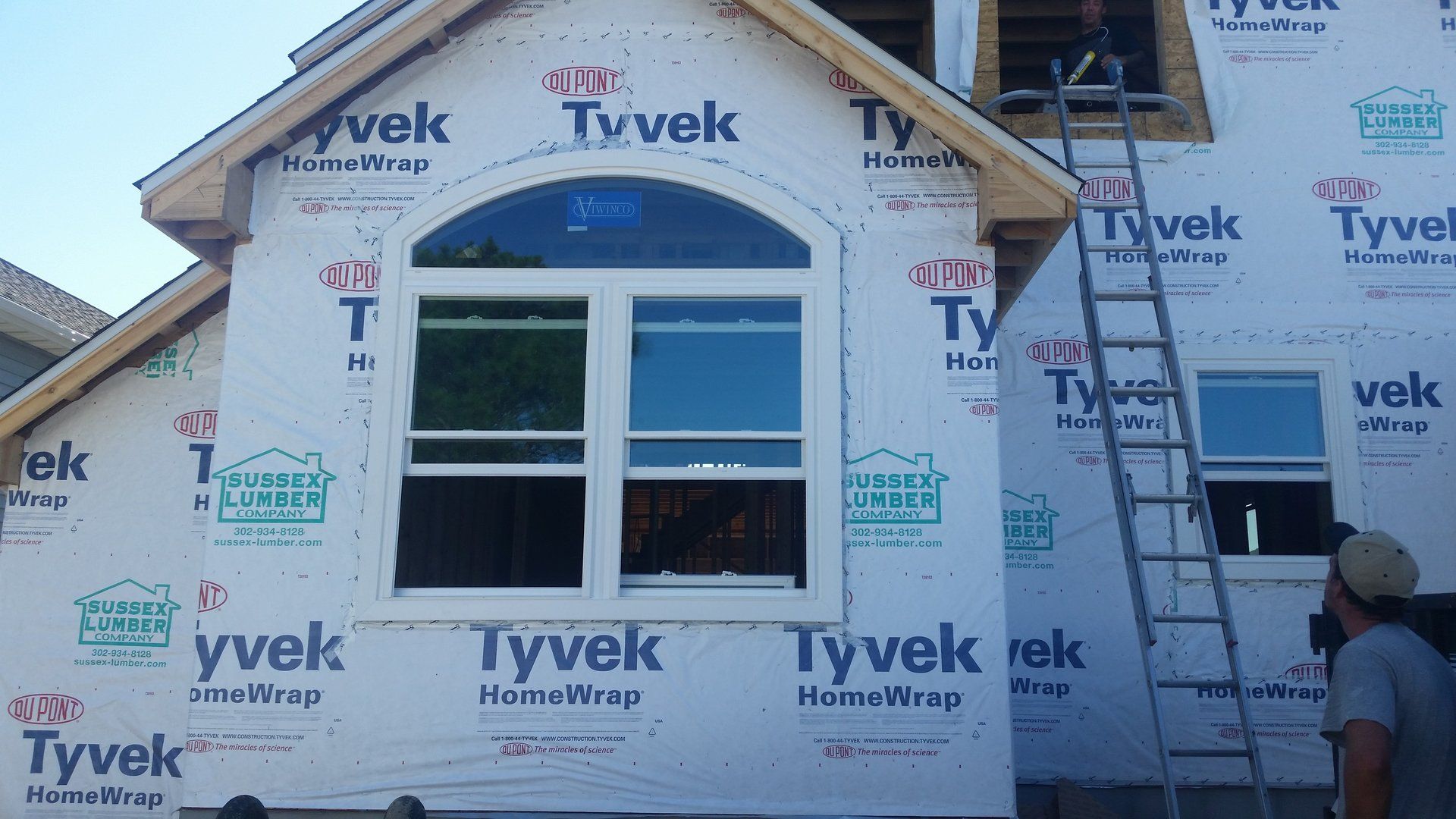 A man is standing on a ladder in front of a house that is being built