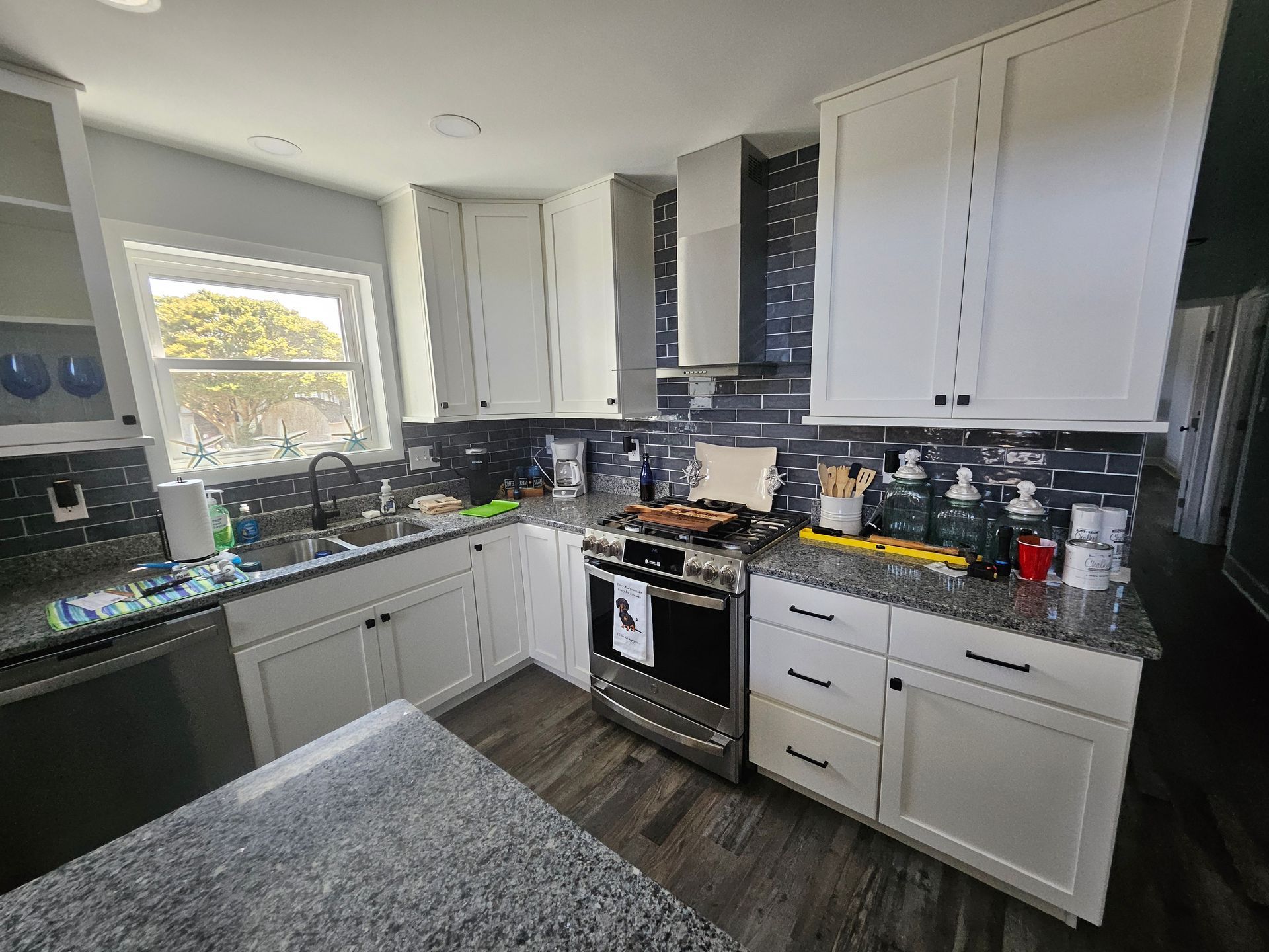 A kitchen with white cabinets, granite counter tops, stainless steel appliances, and a window