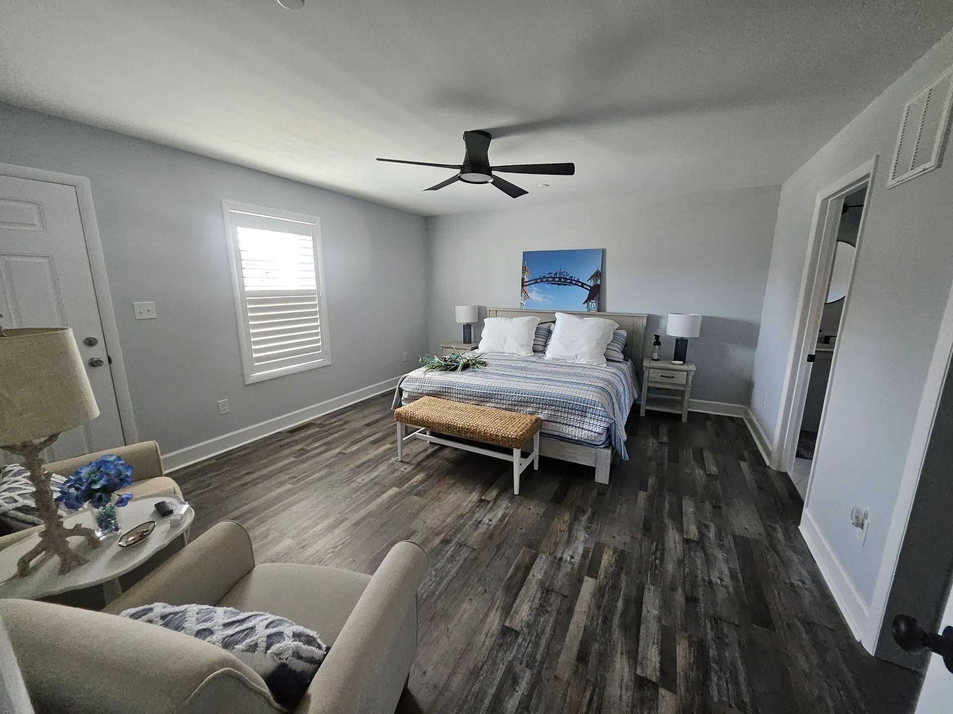 A bedroom with a bed, chair, table, and ceiling fan