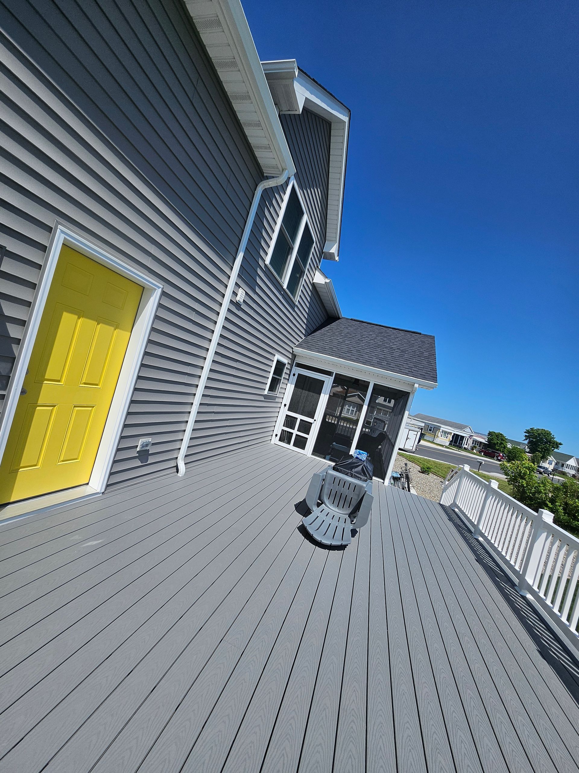 A gray house with a yellow door and a gray deck