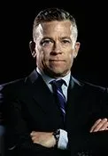 Studio portrait of a man in a dark suit with arms crossed against a black background