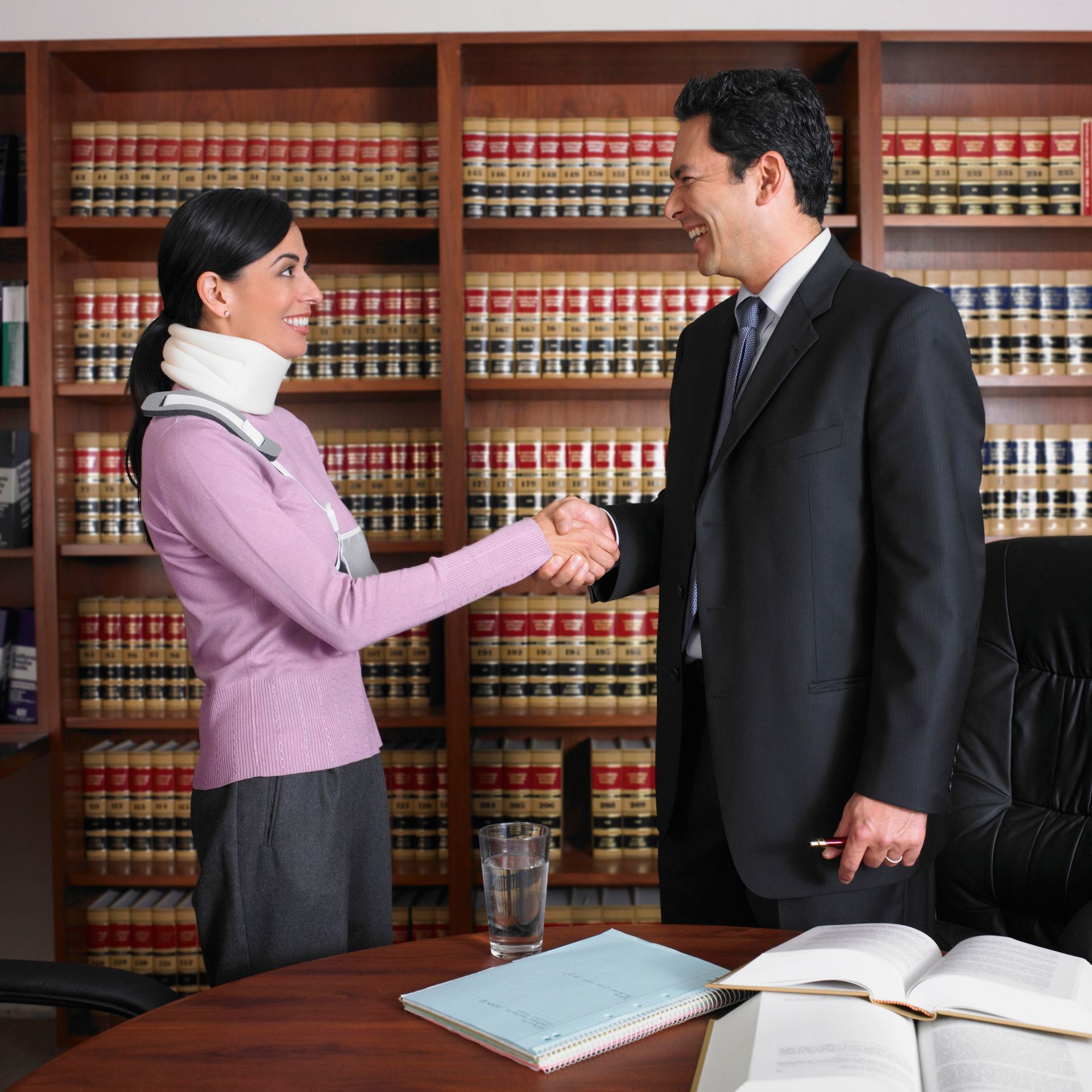 Two business professionals shaking hands in an office library with law books on the shelves.