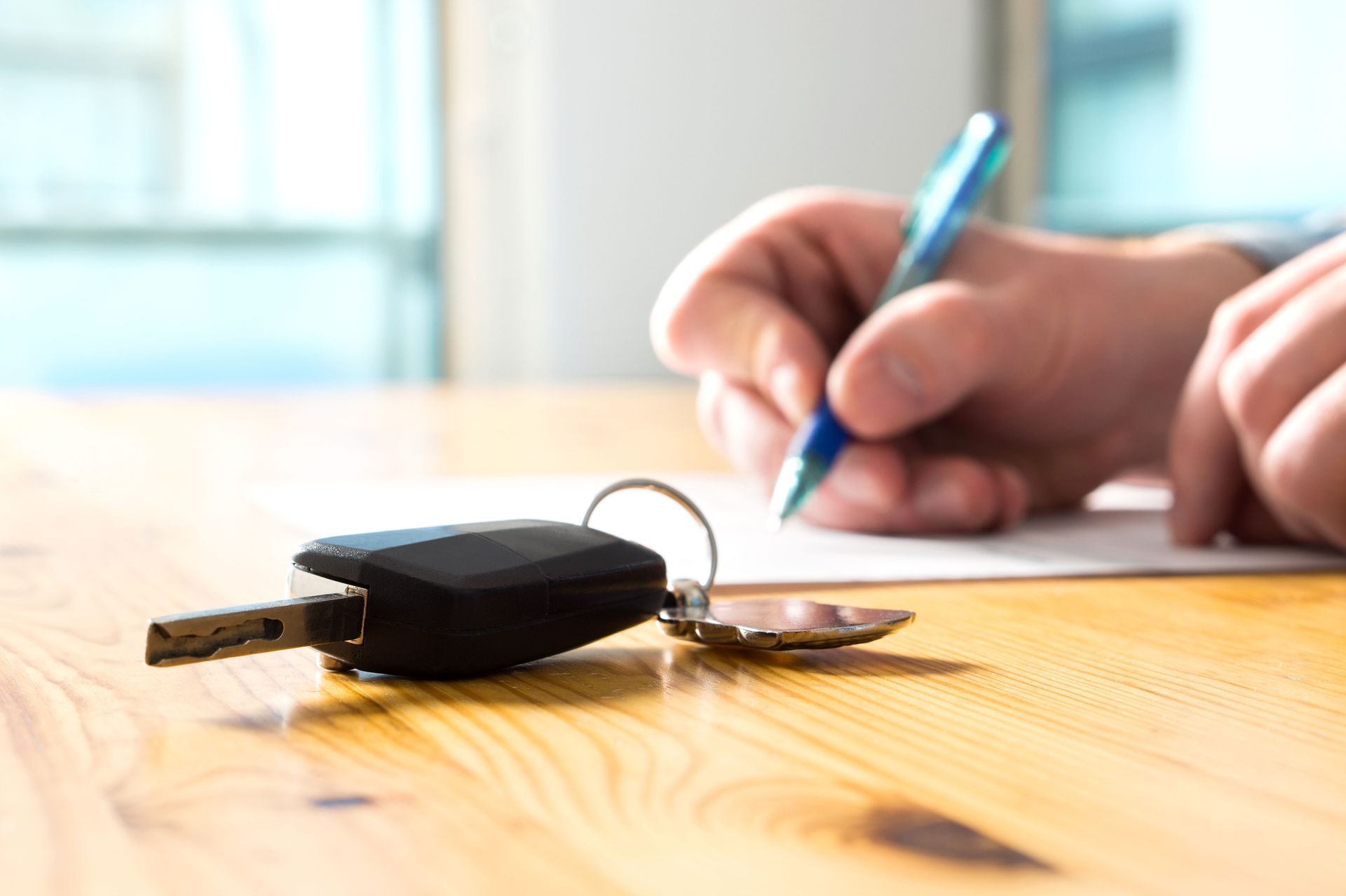 Car keys on a table beside a hand writing in a notebook