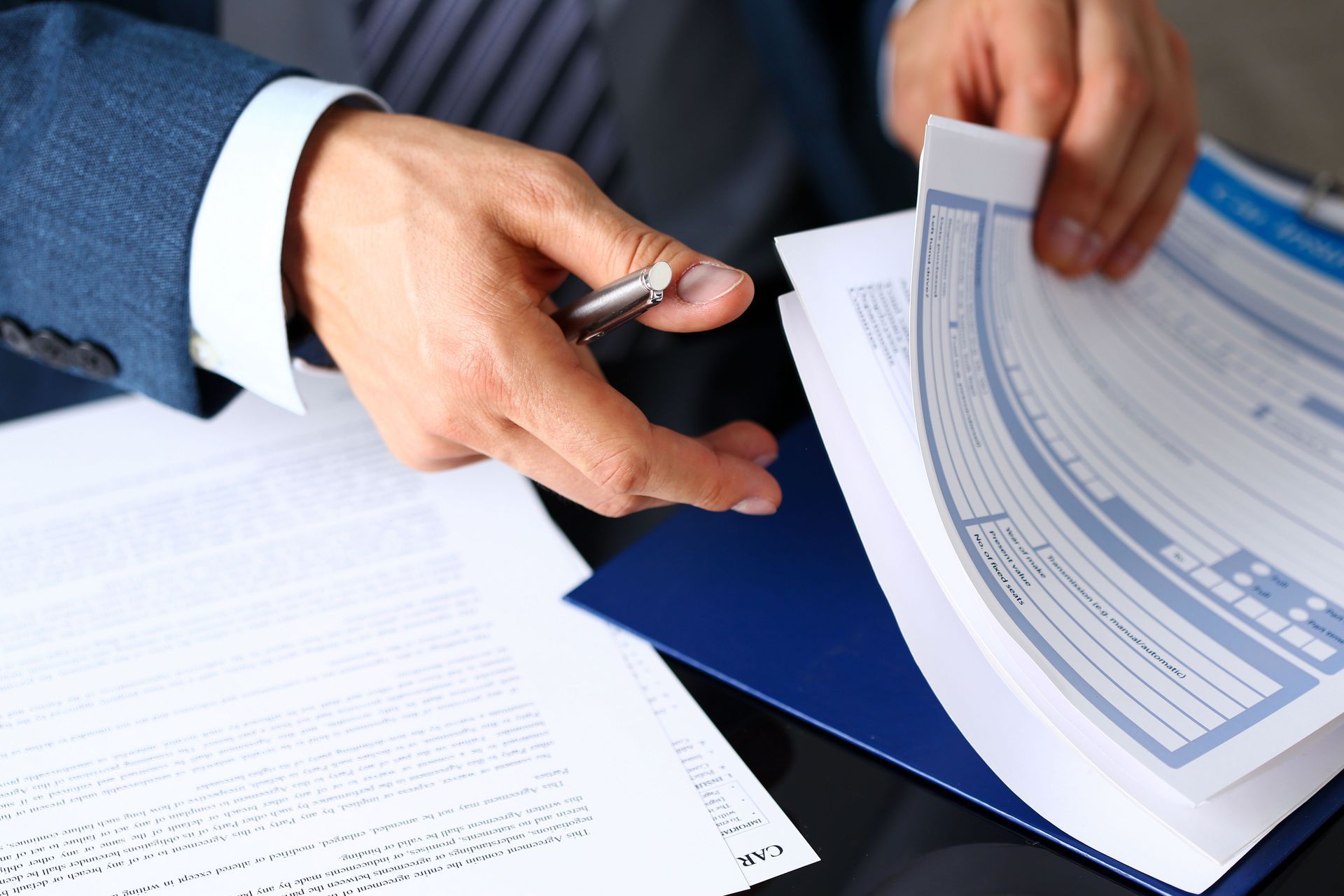 Businessperson holding a pen over documents and a blue folder during a paperwork review