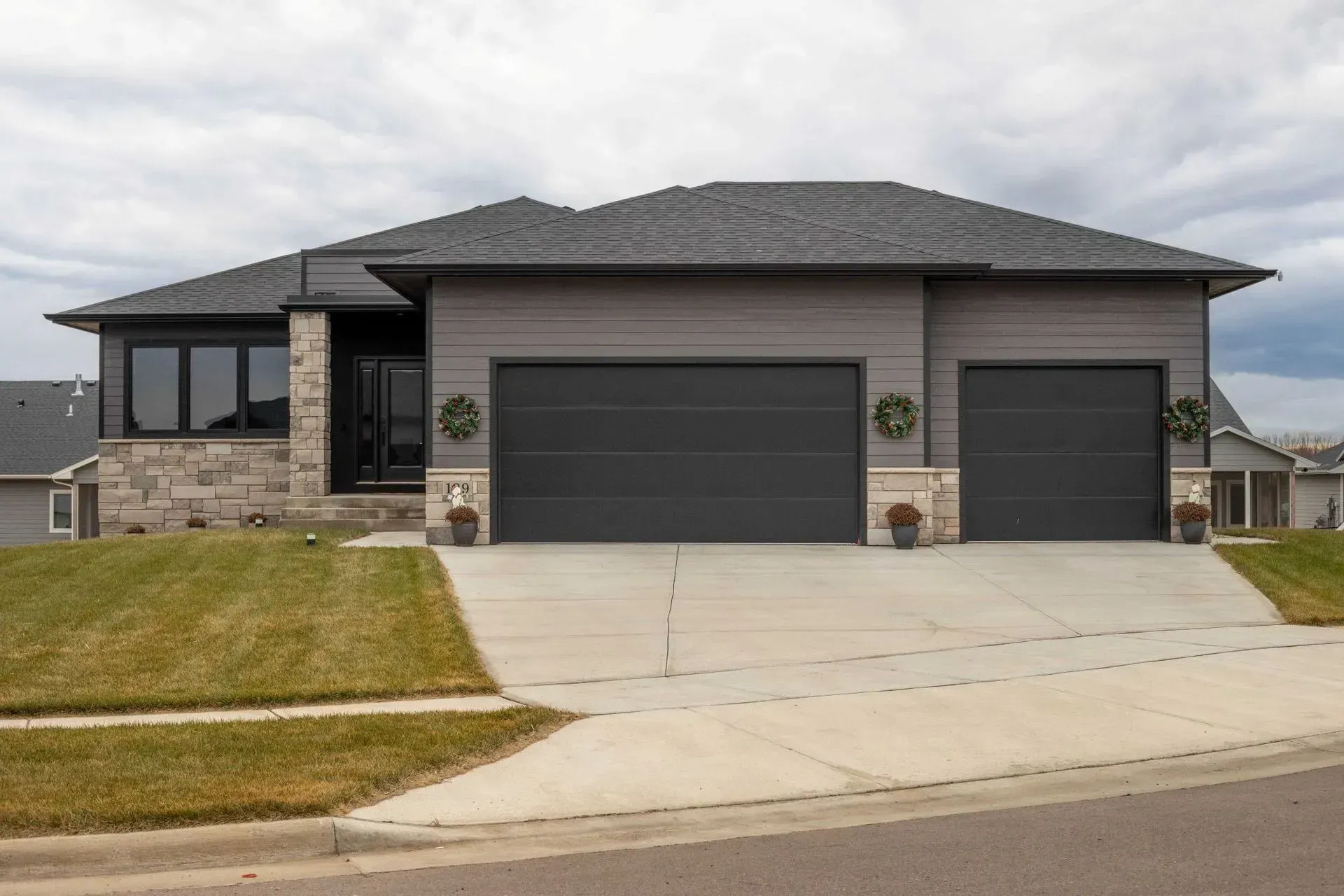 Modern gray house with two-car garage, stone facade, and a cloudy sky.