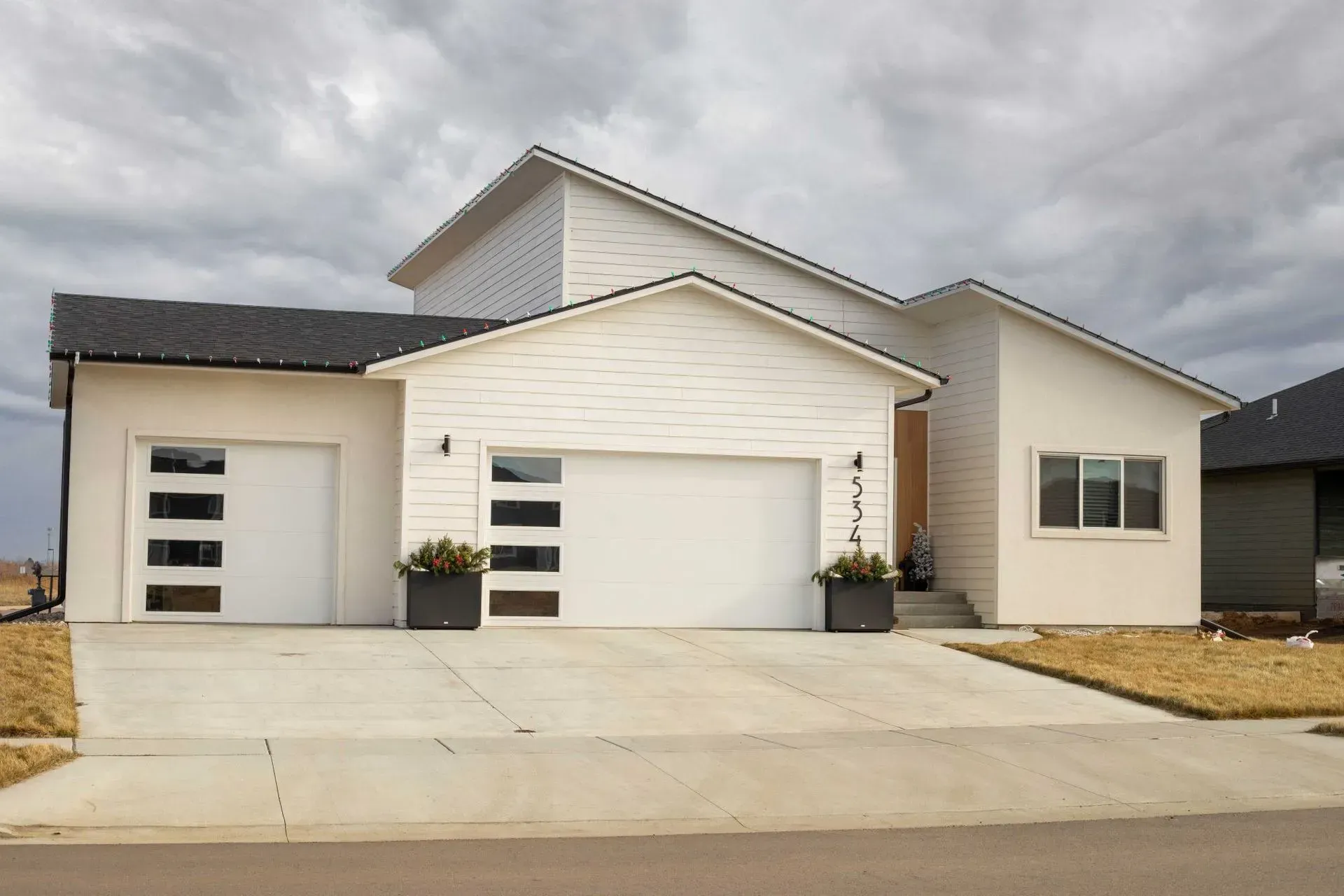 White modern house with two-car garage, concrete driveway, and gray cloudy sky.