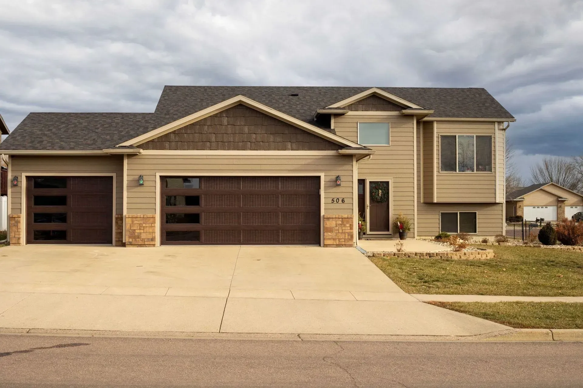 Tan two-story house with dark brown garage doors, set against a cloudy sky.