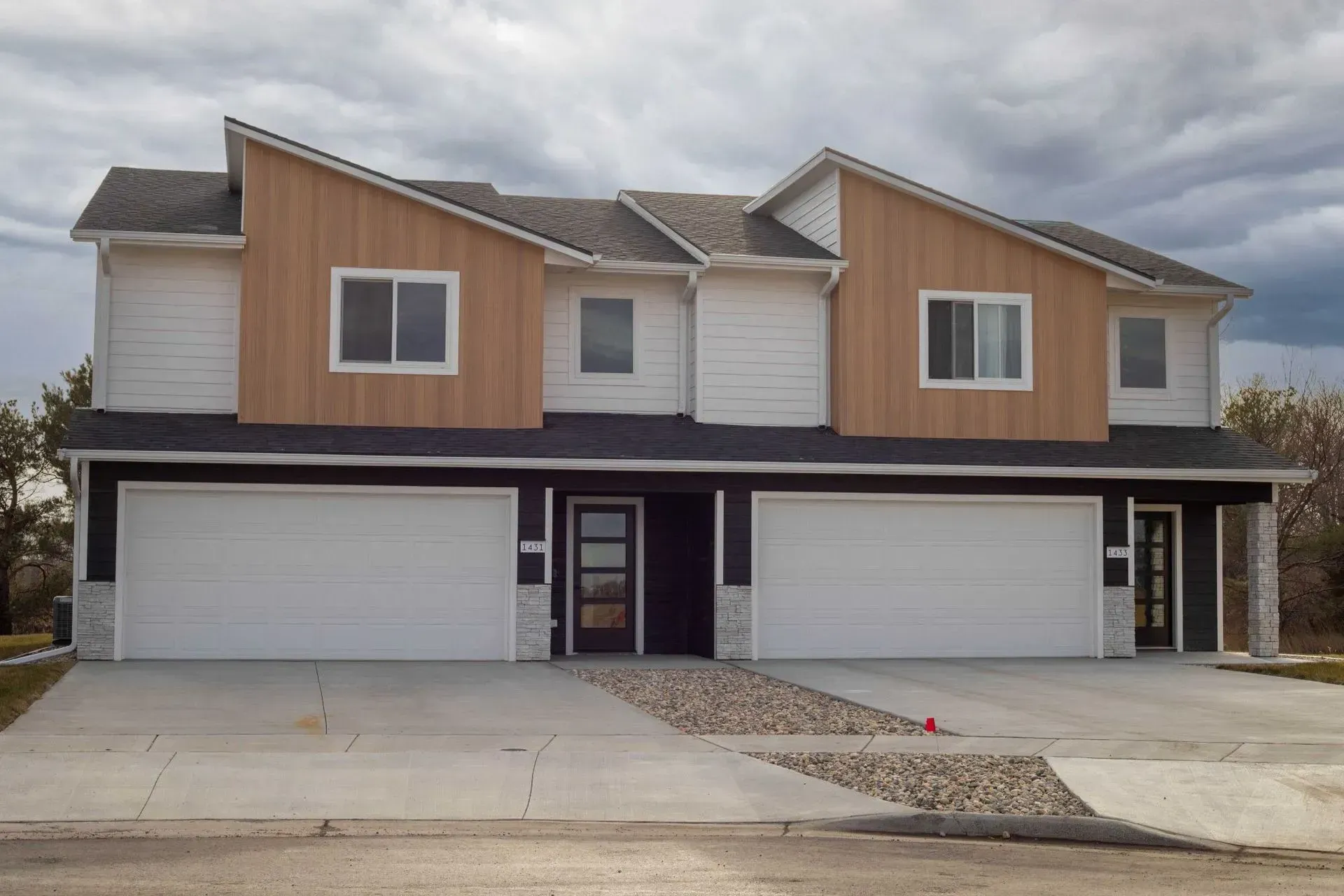 Two-unit townhouse with white and wood siding, two garage doors, and a concrete driveway.