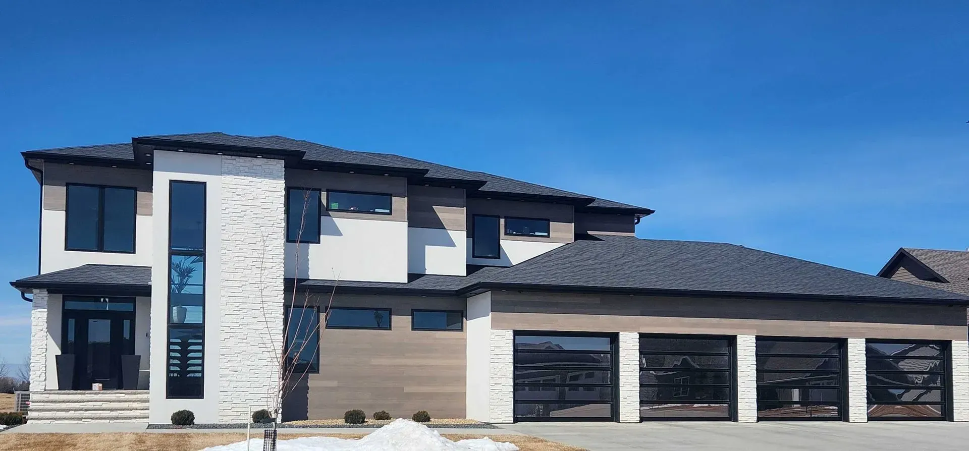 Modern two-story house with stone facade, glass garage doors, and a clear blue sky.
