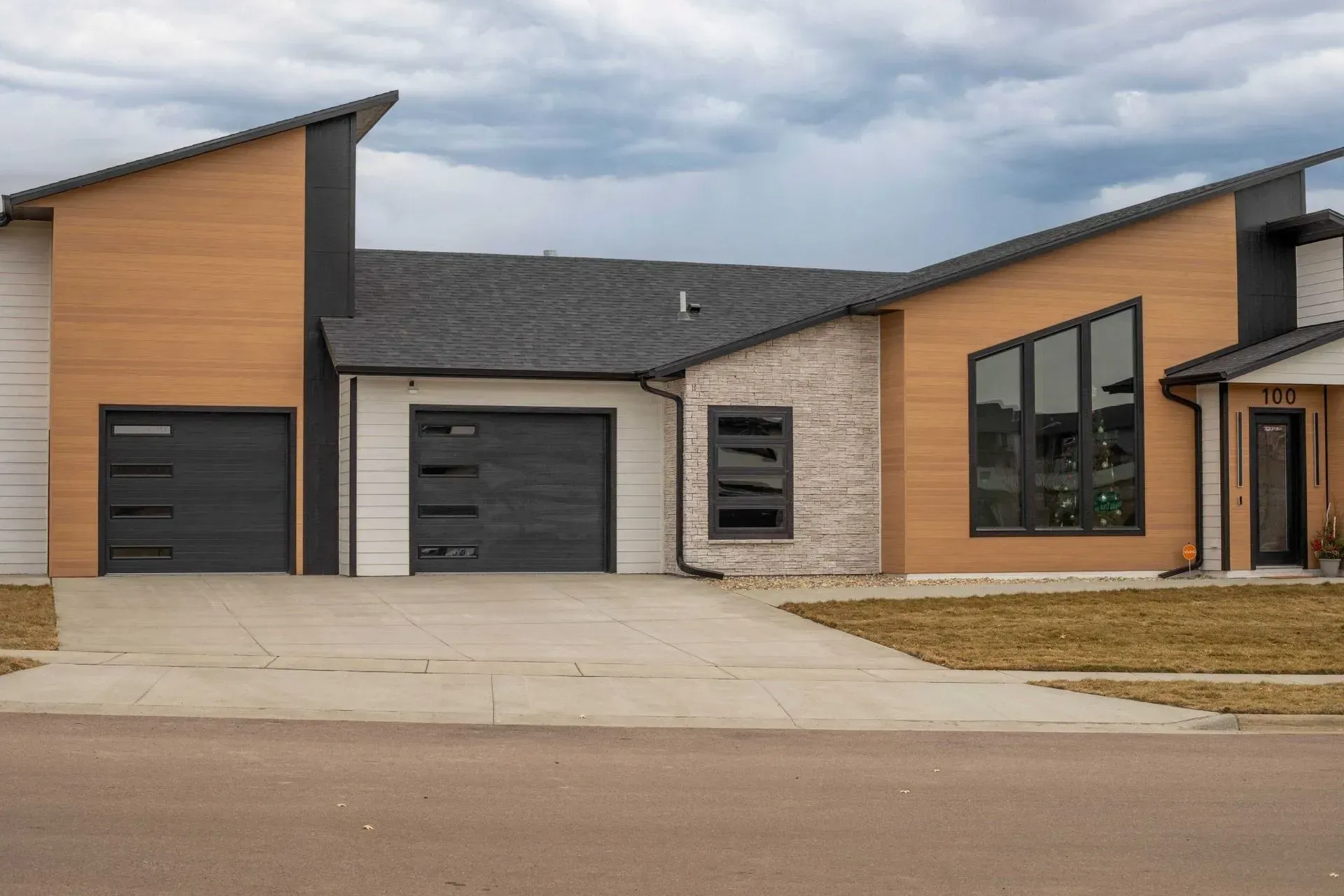 Modern home exterior with asymmetrical roof, garage doors, and diverse facade materials.