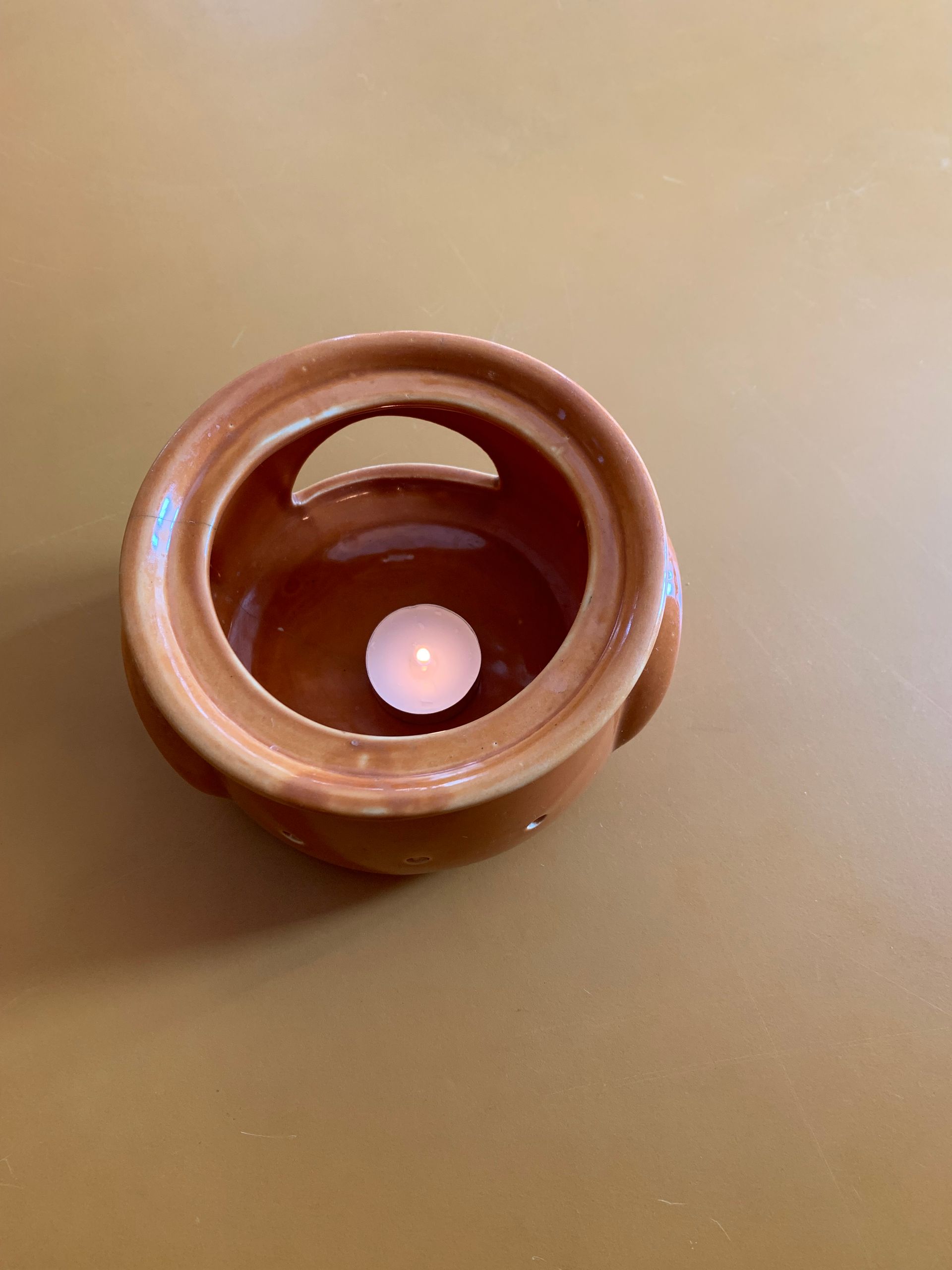 A brown bowl with a candle in it is on a table