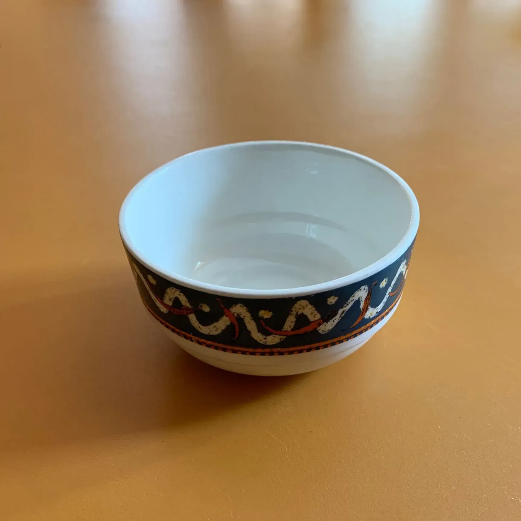 A small white bowl with a blue and gold border sits on a table