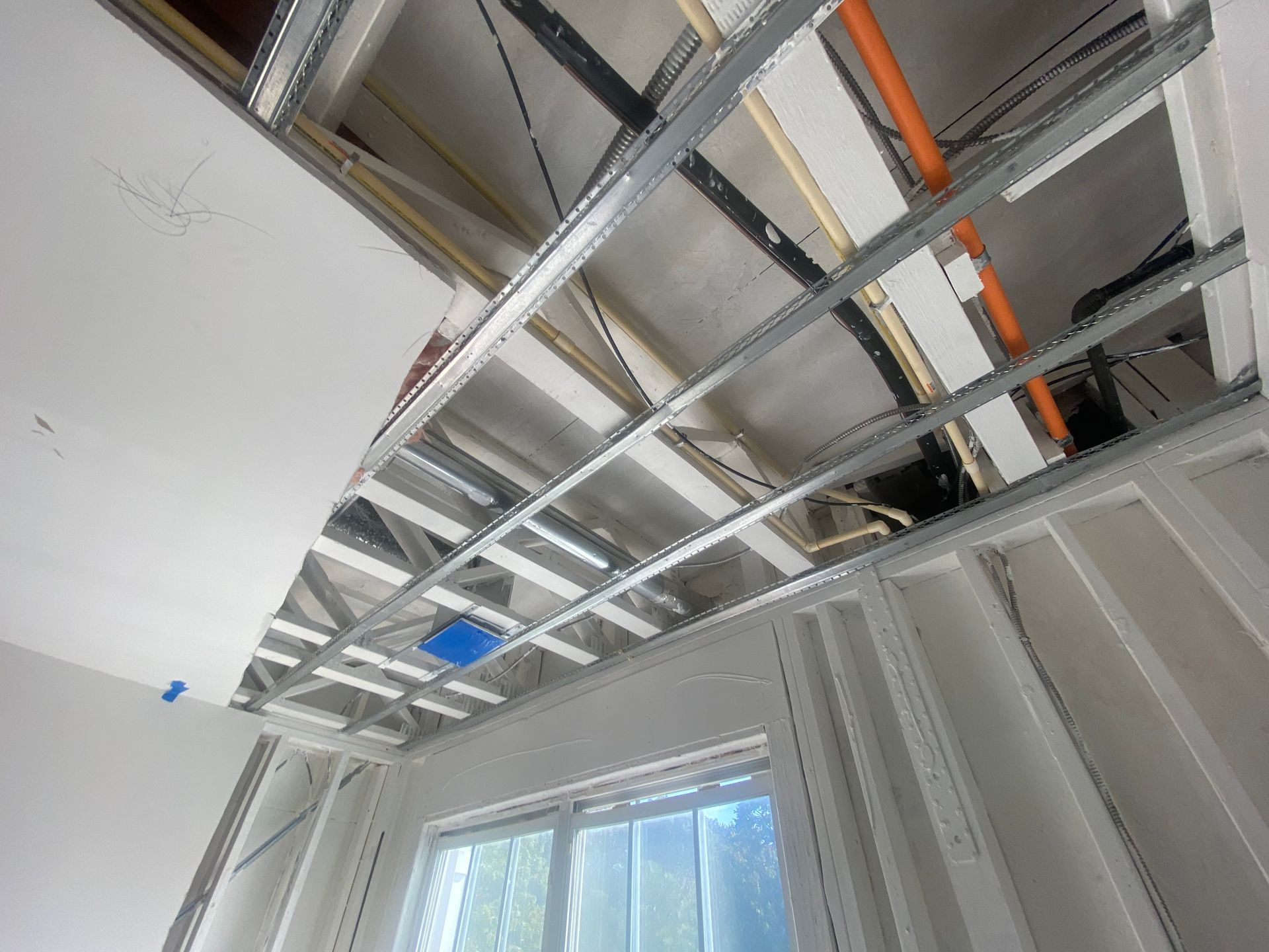 Interior view of unfinished construction showing a metal ceiling grid, wall studs, drywall sections, and exposed piping.