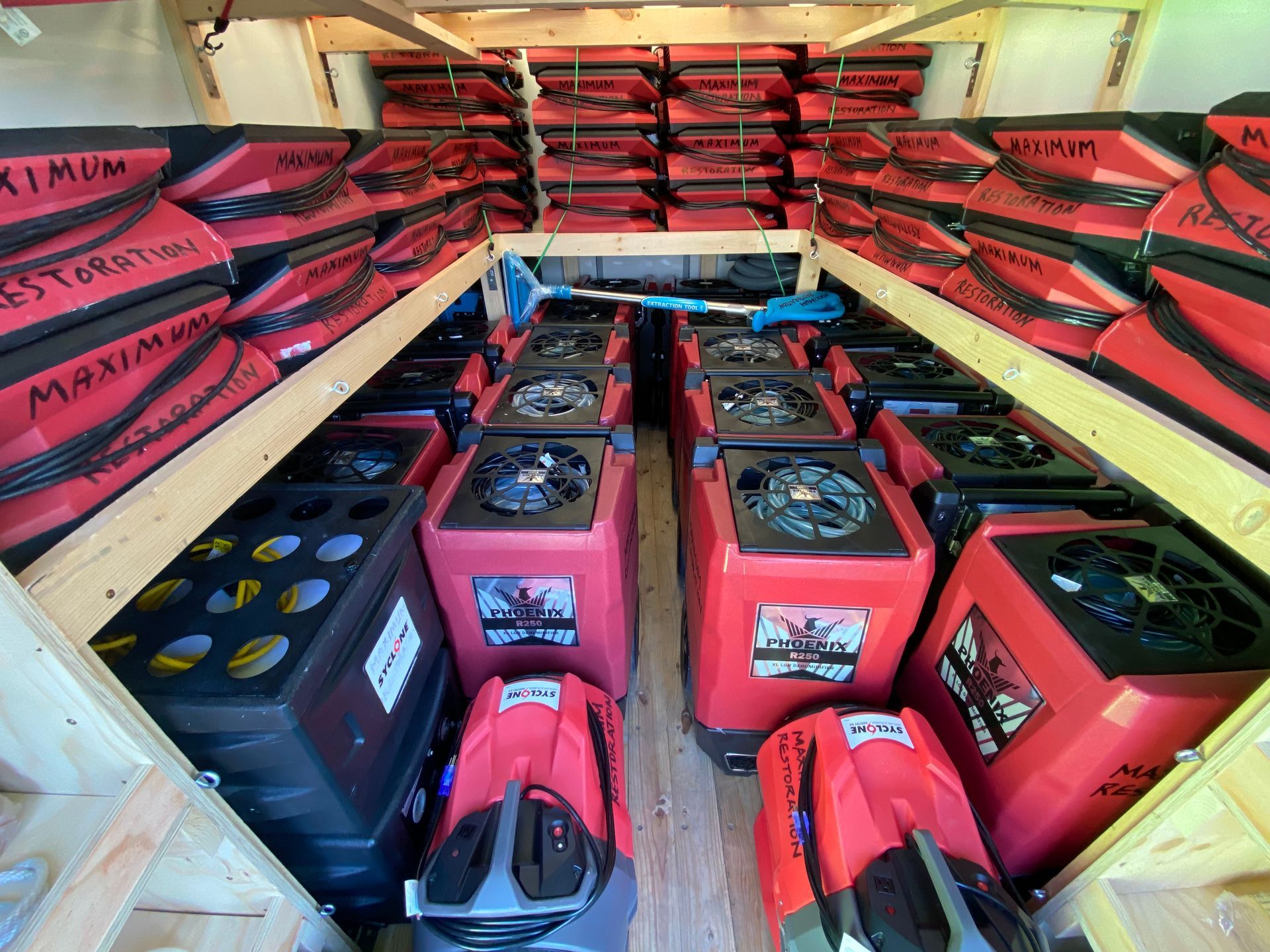 A cargo area filled with stacked rows of red industrial air movers and dehumidifiers on wooden shelving.