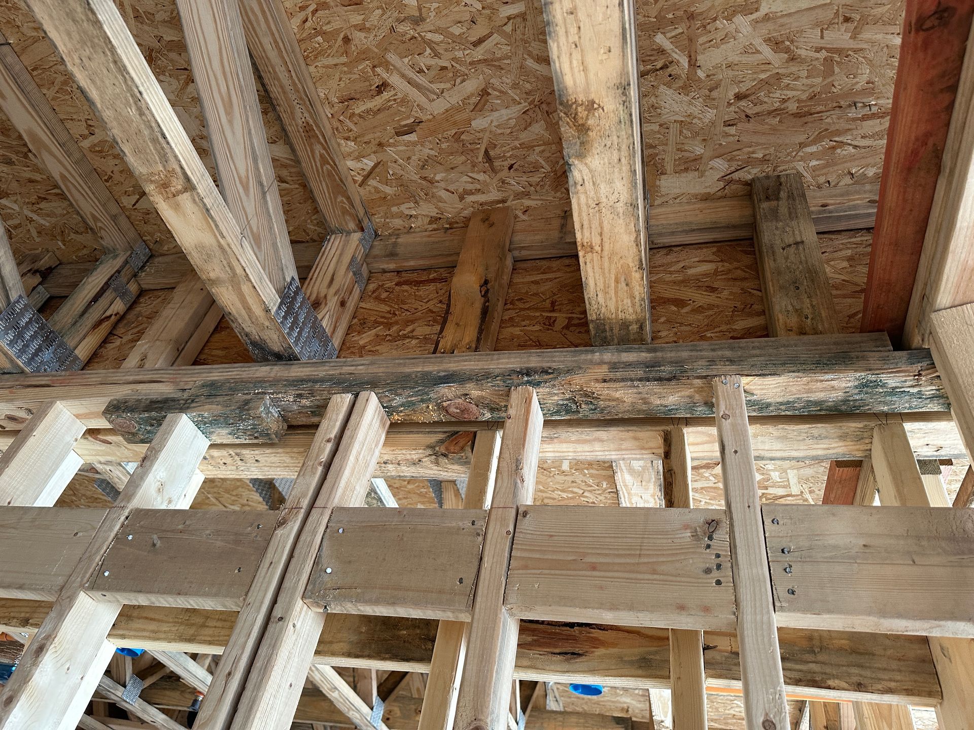 A close-up view of unfinished wooden framing, floor joists, and plywood subflooring inside a residential construction site.
