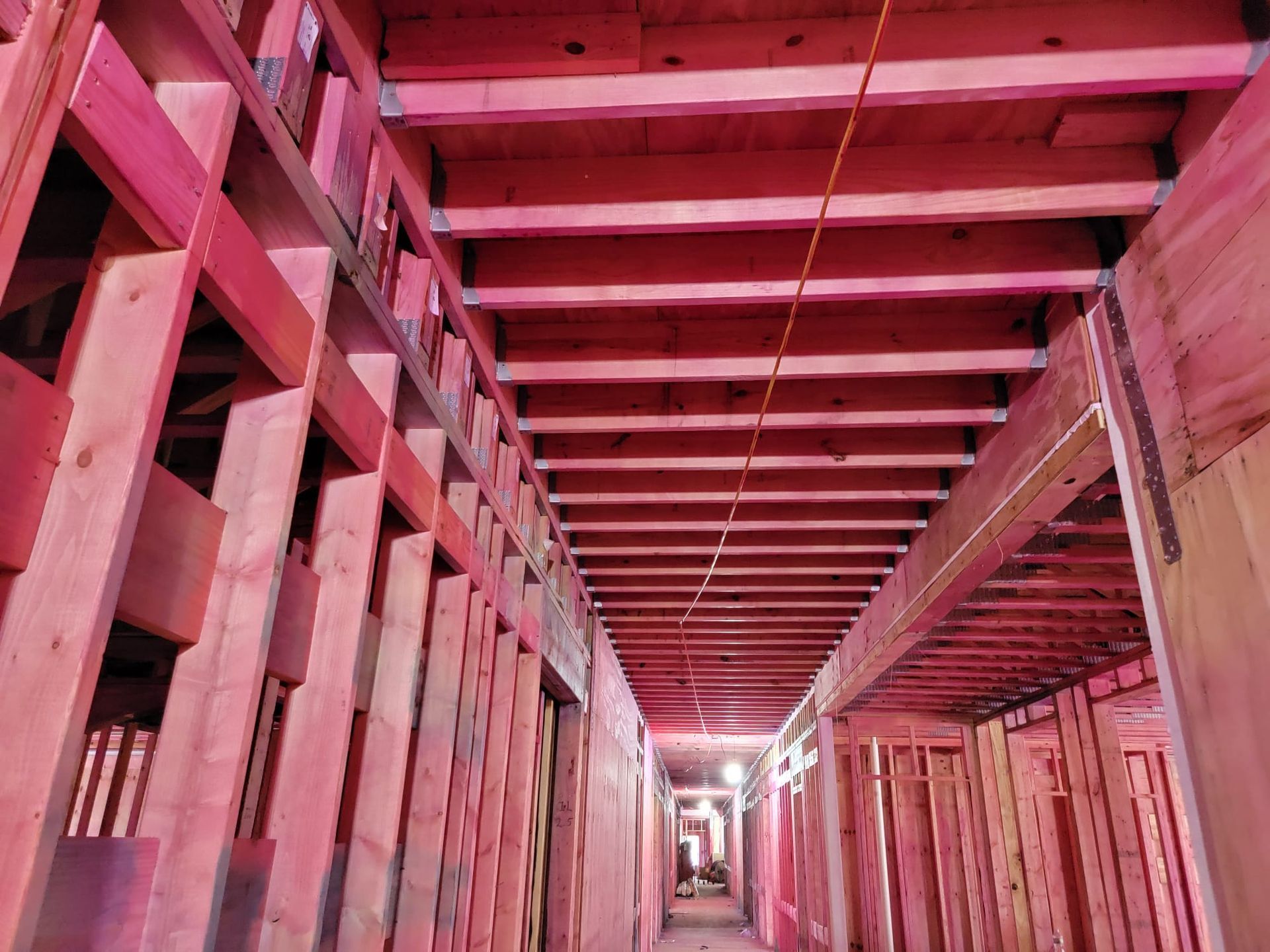 Wooden framework of a hallway under construction. Red-toned lighting illuminates the beams and studs.