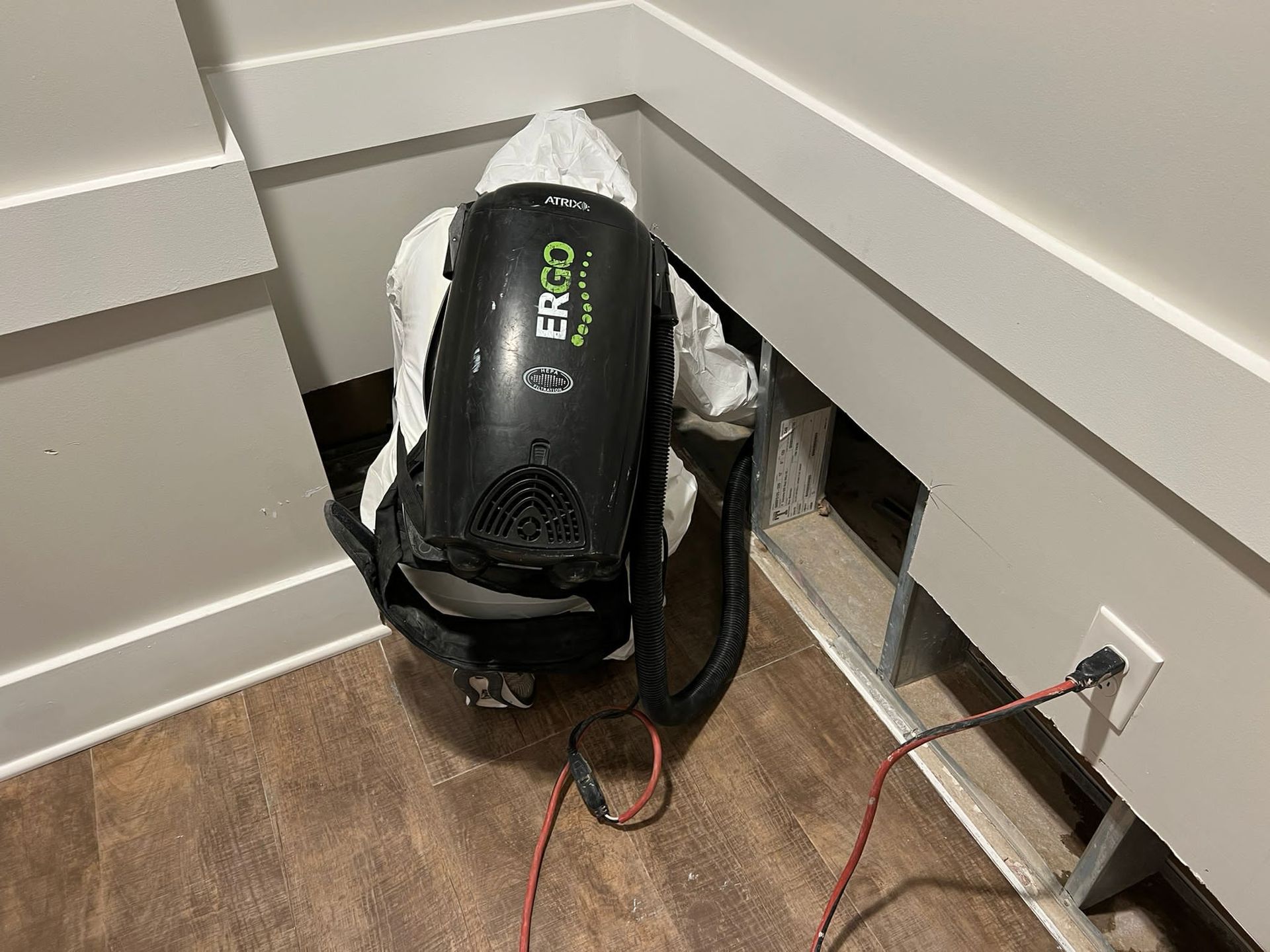 Person in protective suit, backpack sprayer entering a hole in a wall, near electrical outlet, and flooring.