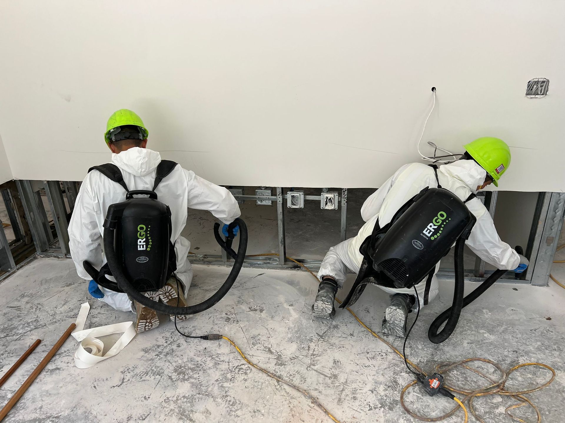 Two workers in protective suits vacuuming a construction site.