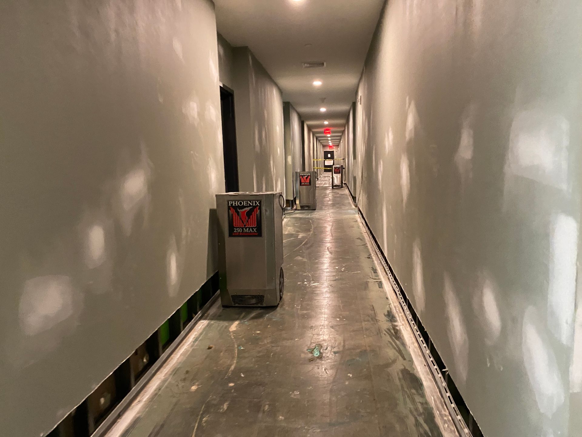 Long, unfinished hallway with drywall, repair machines, and exposed construction.