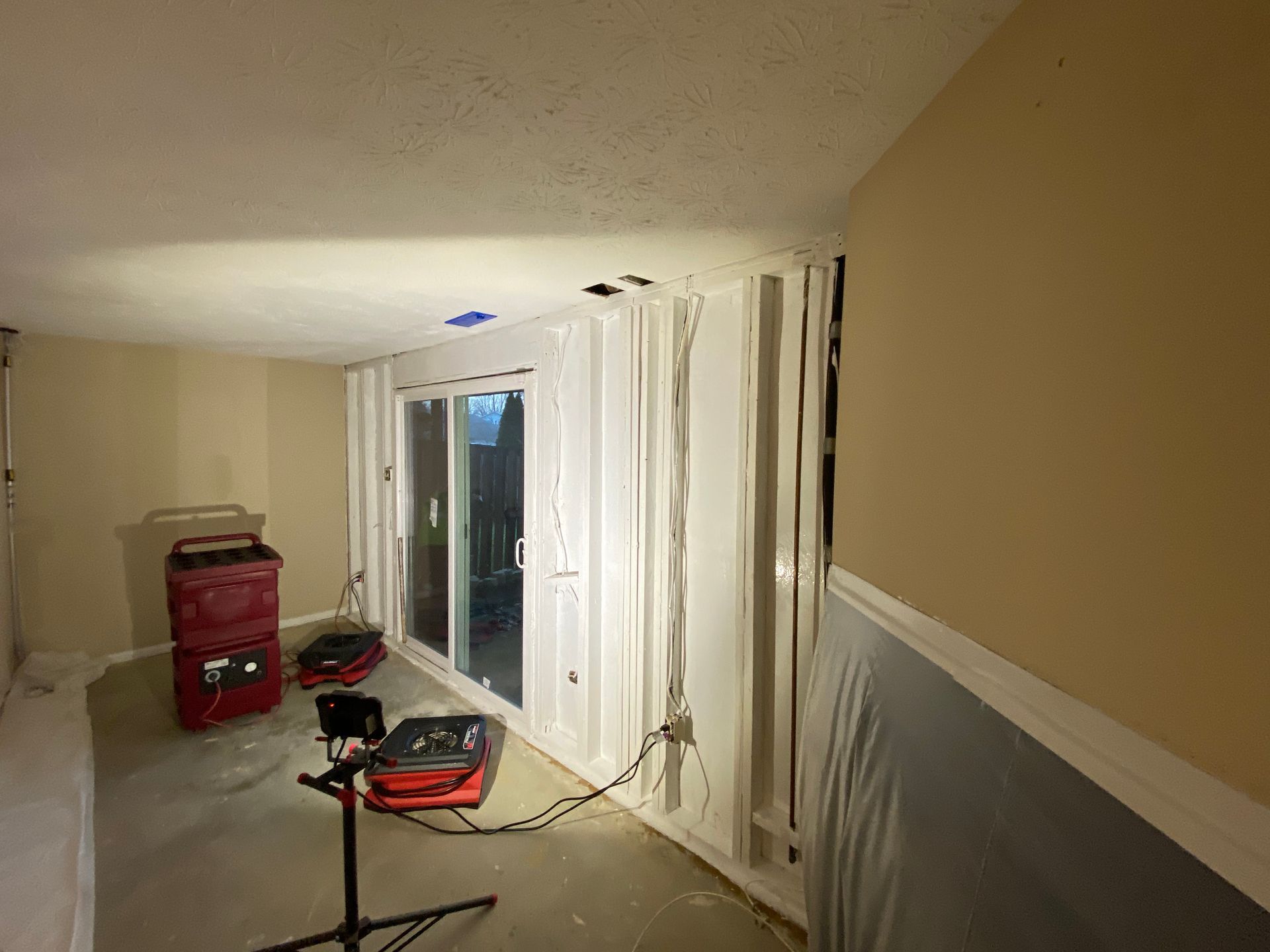 Basement undergoing renovation; exposed wiring, sliding glass door, and work lights visible.