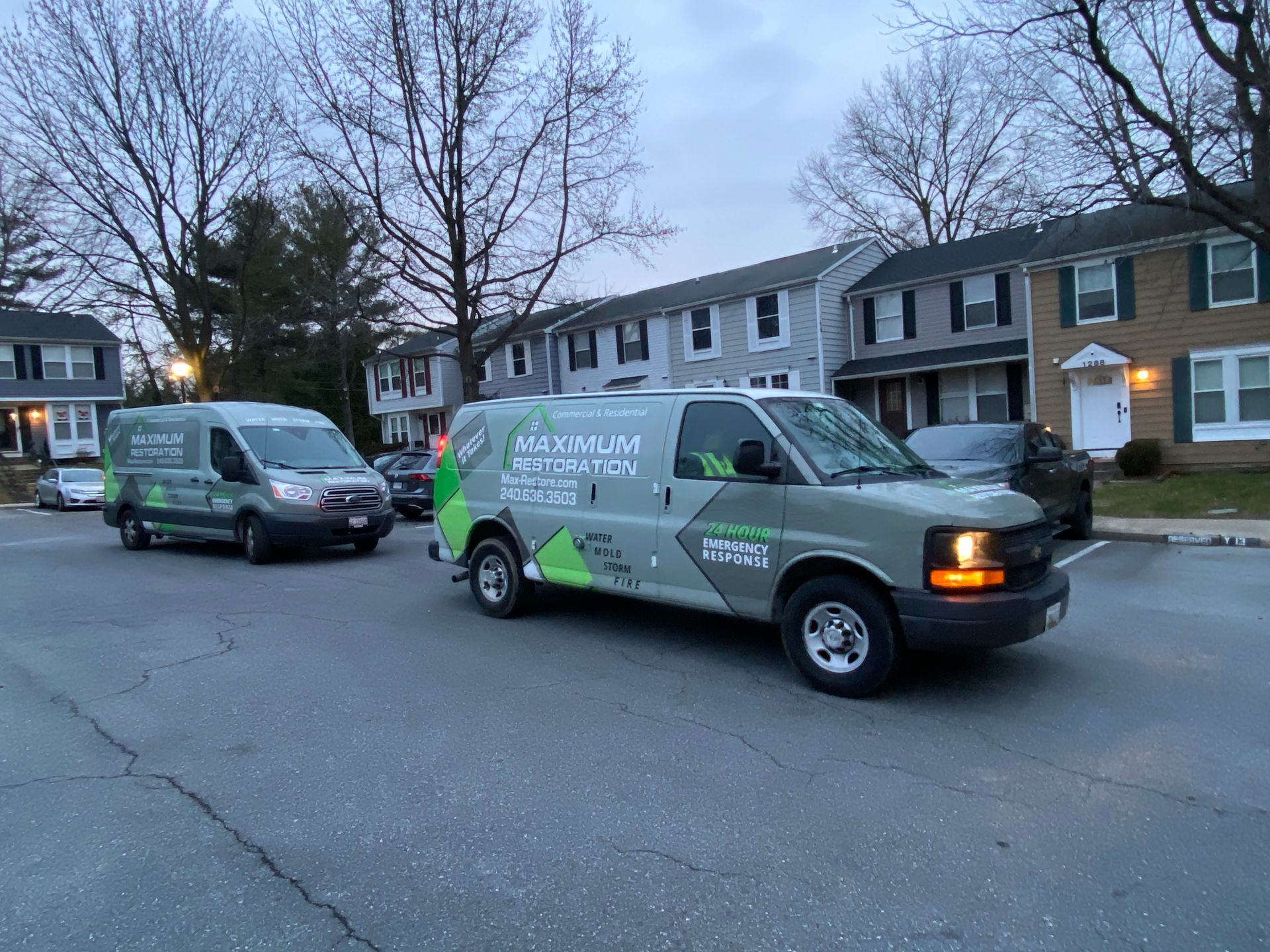 Two green and gray service vans parked on a residential street.