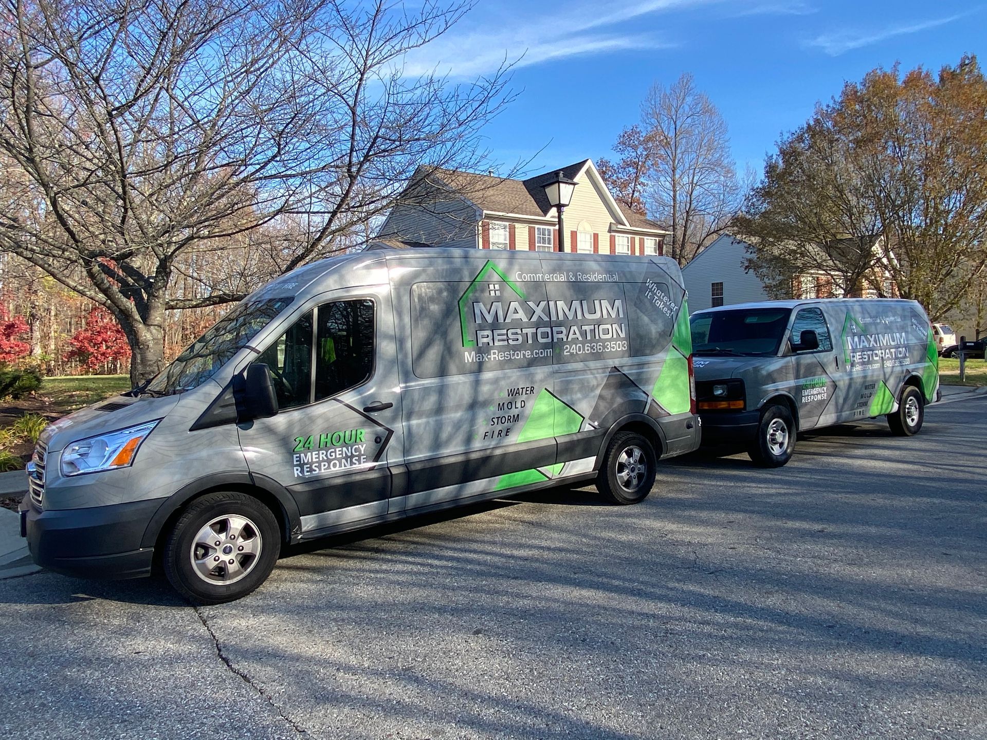 Two gray service vans parked on a residential street. Vans have green and black logos and text.