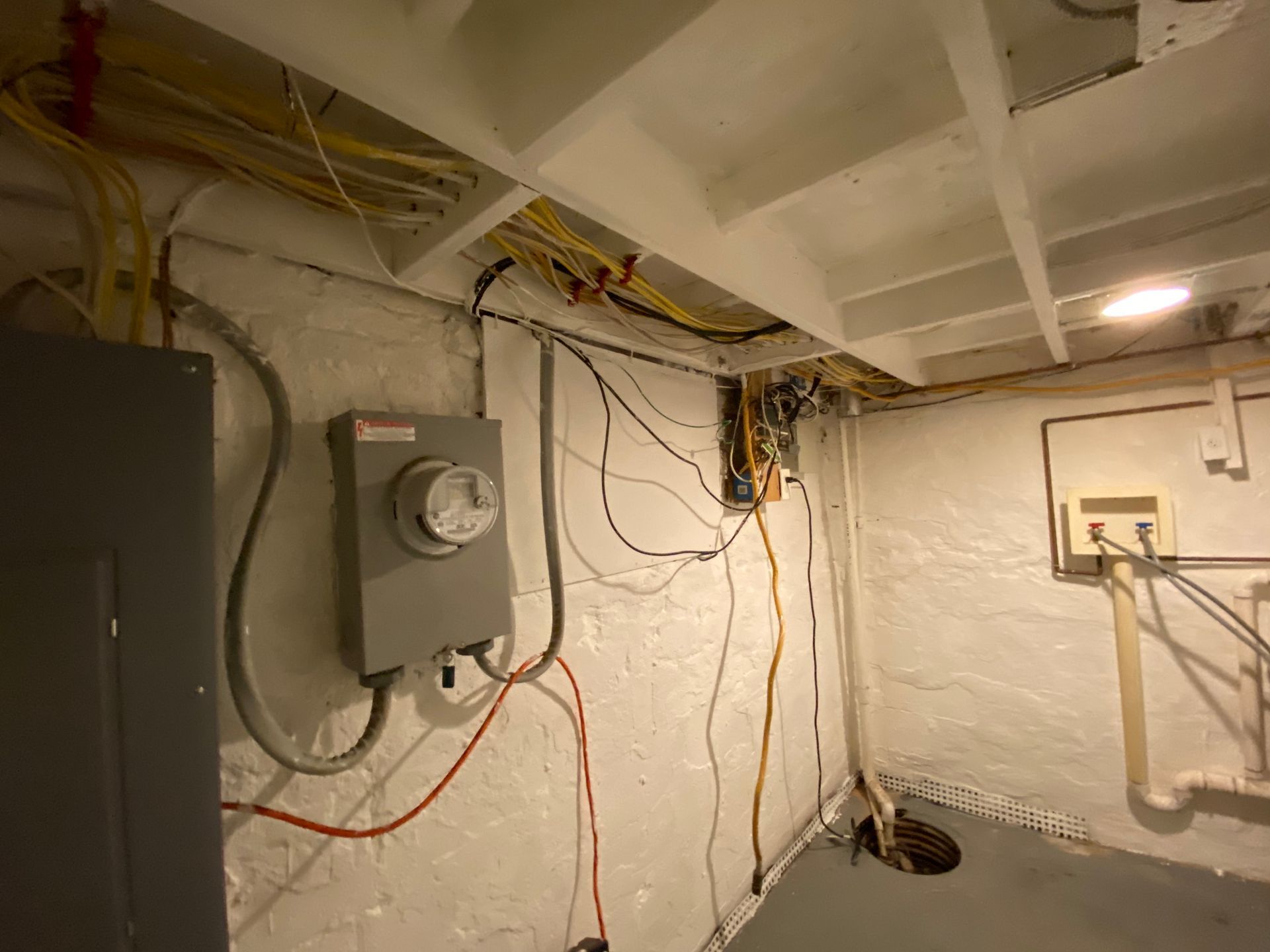 Electrical panel, meter, and wiring in a basement, with exposed wires and a white painted ceiling.