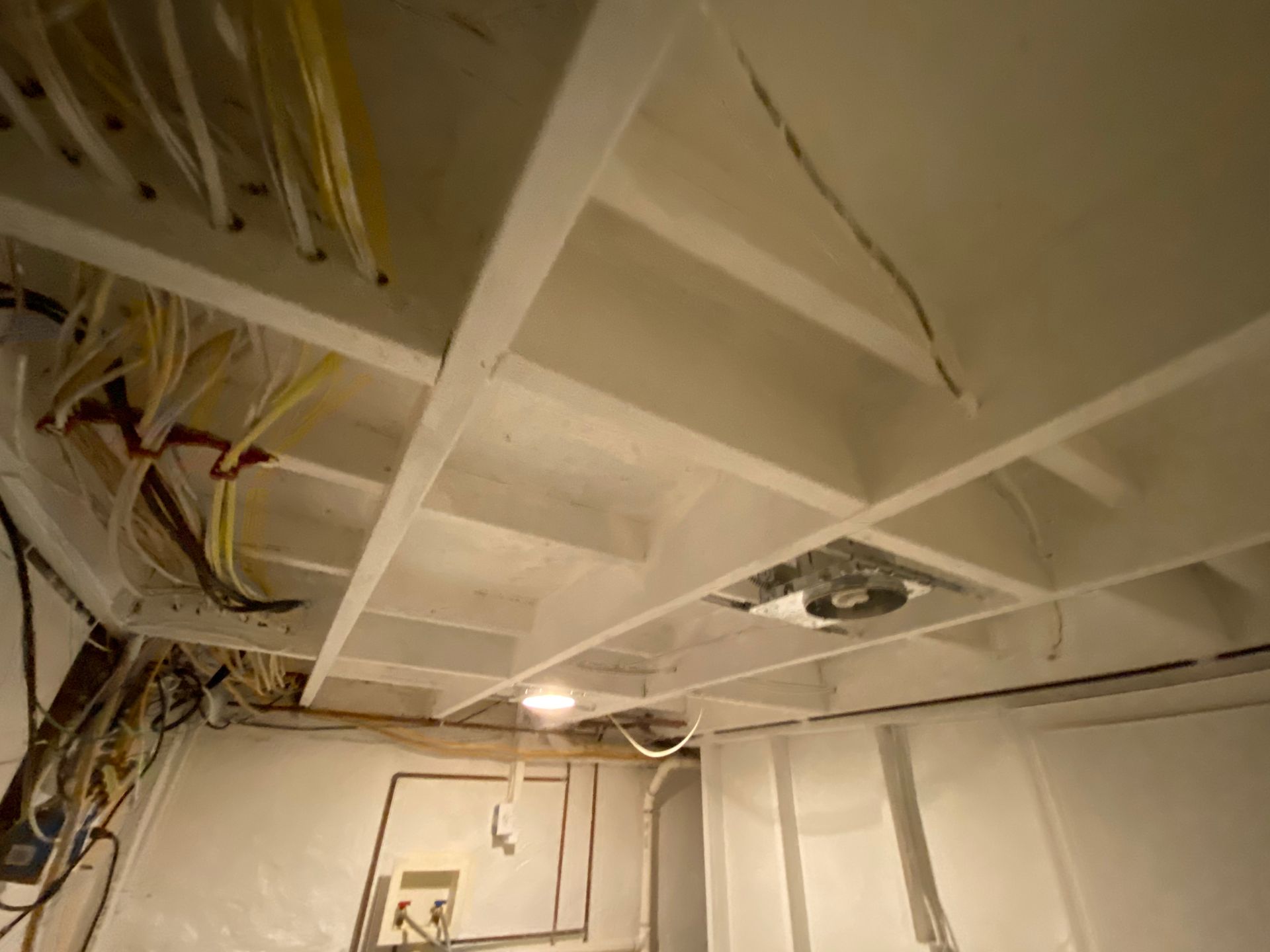 White ceiling with exposed beams, wiring, and a ventilation fan.