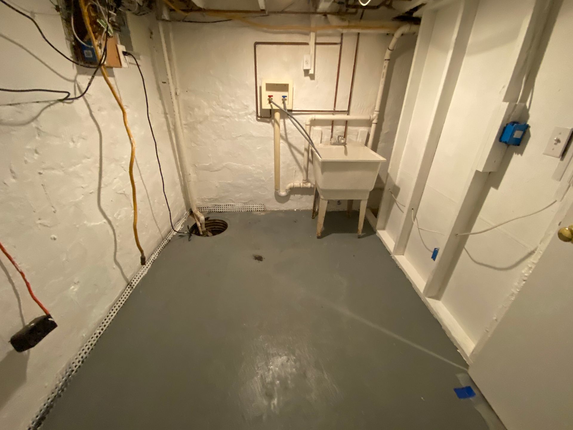 Basement laundry area with white walls, gray floor, utility sink, and exposed wiring.
