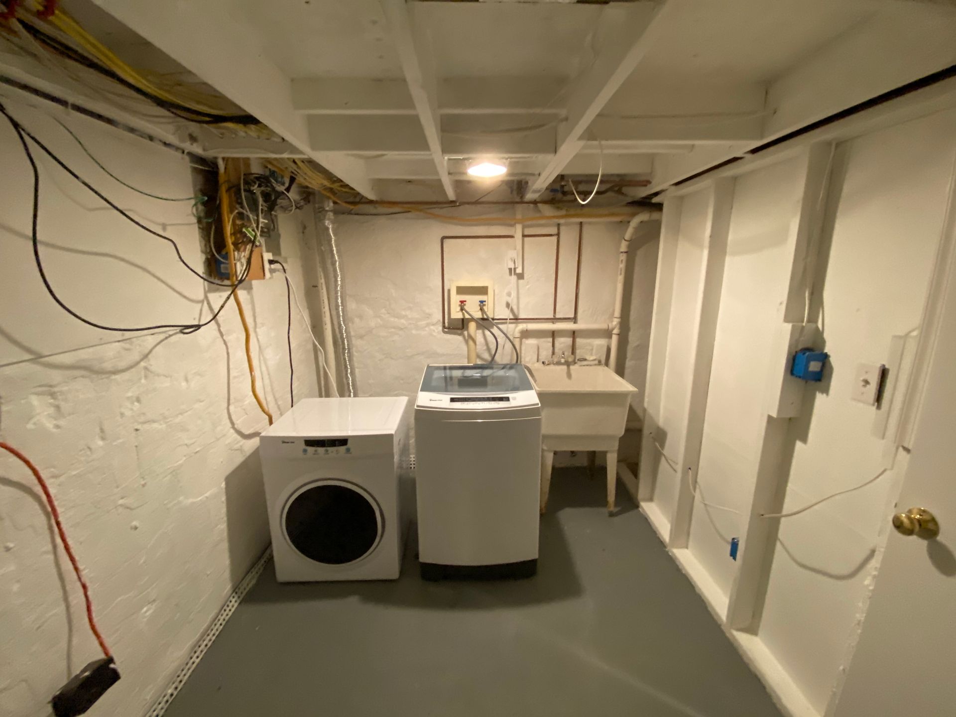 Laundry room with washer, dryer, utility sink, and electrical panel; white walls, gray floor.