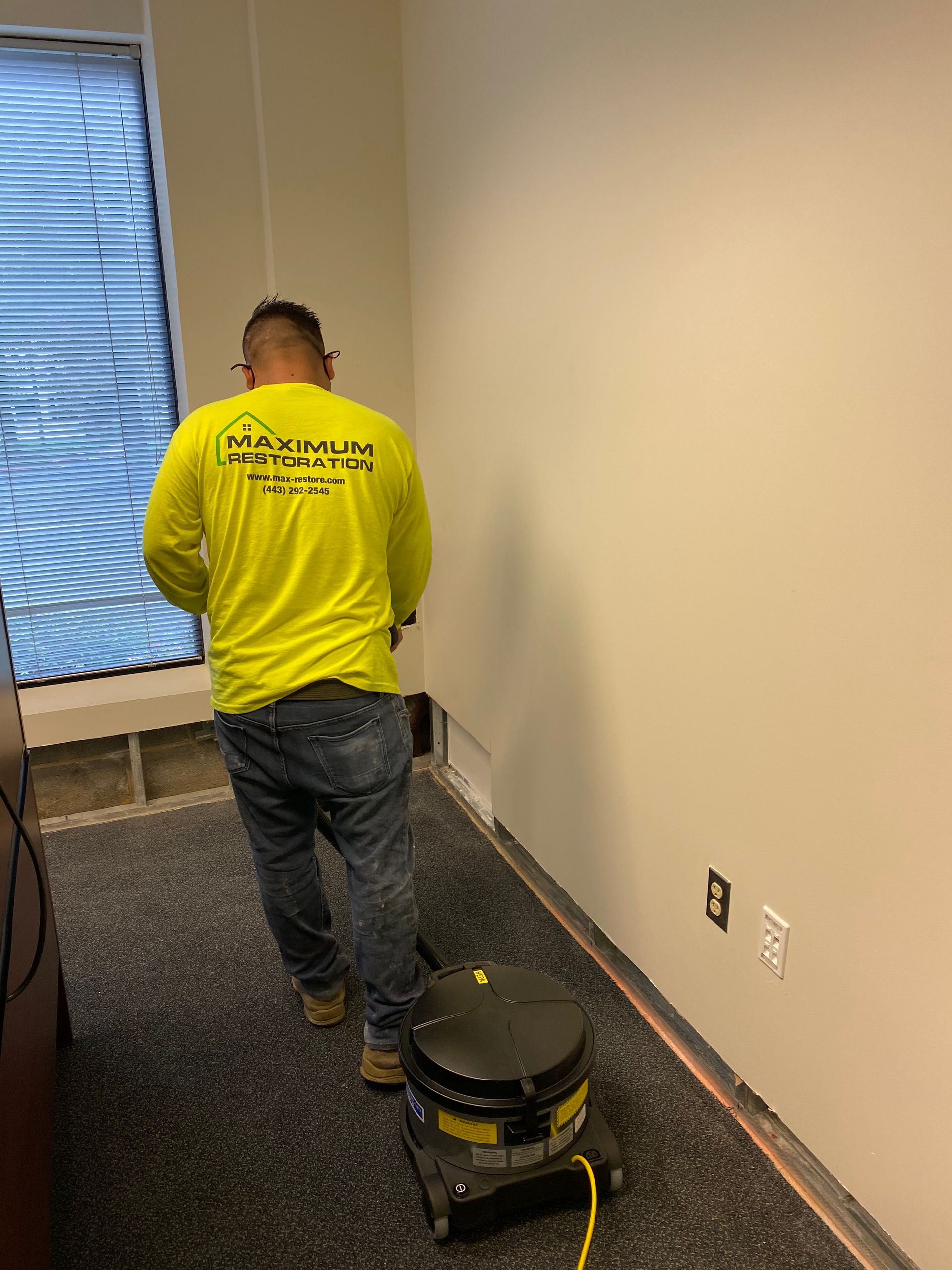 Person using floor sanding machine in a room with a window, beige walls, and dark flooring.